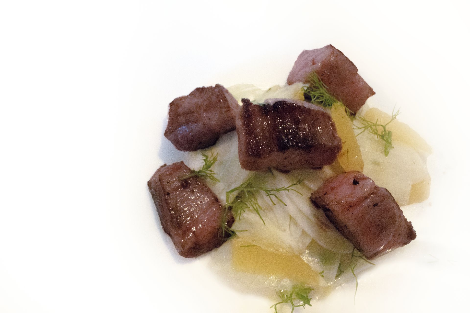 Cubetti di manzo scottati con cipolle trasparenti ed erbe aromatiche su un piatto bianco