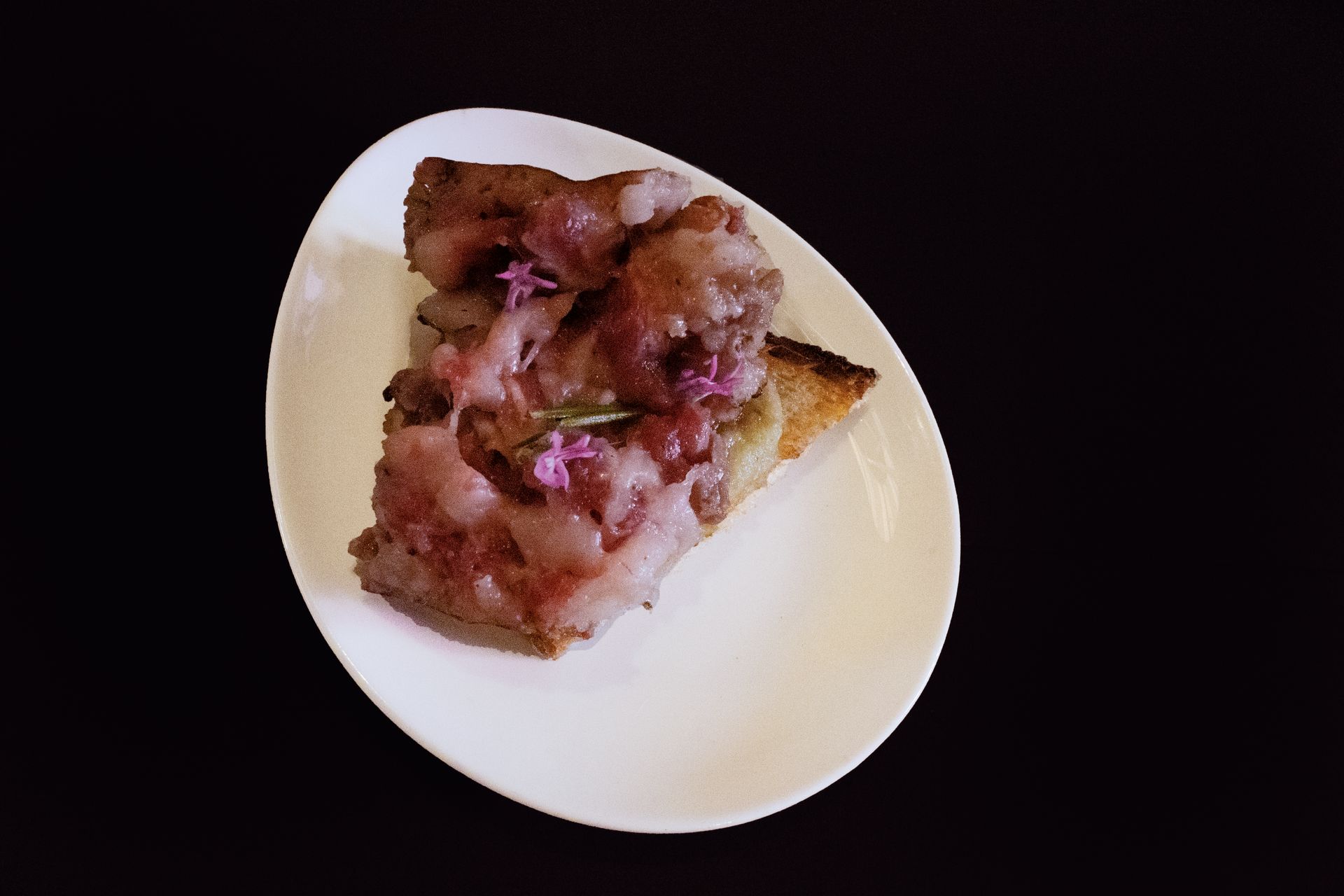 Una fetta di pizza su un piatto bianco su uno sfondo scuro