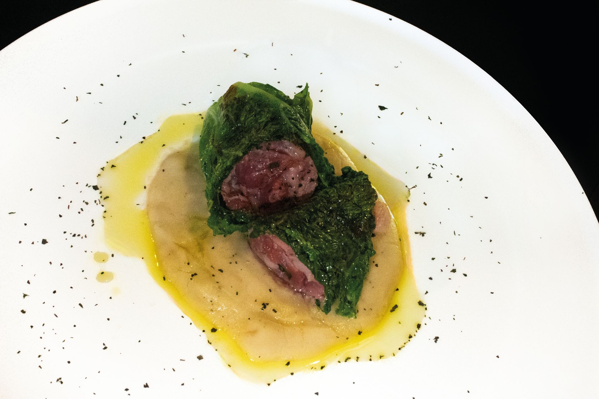 Antipasto con carne rossa in crosta di erbe aromatiche, servito su un piatto bianco e condito con una salsa gialla.