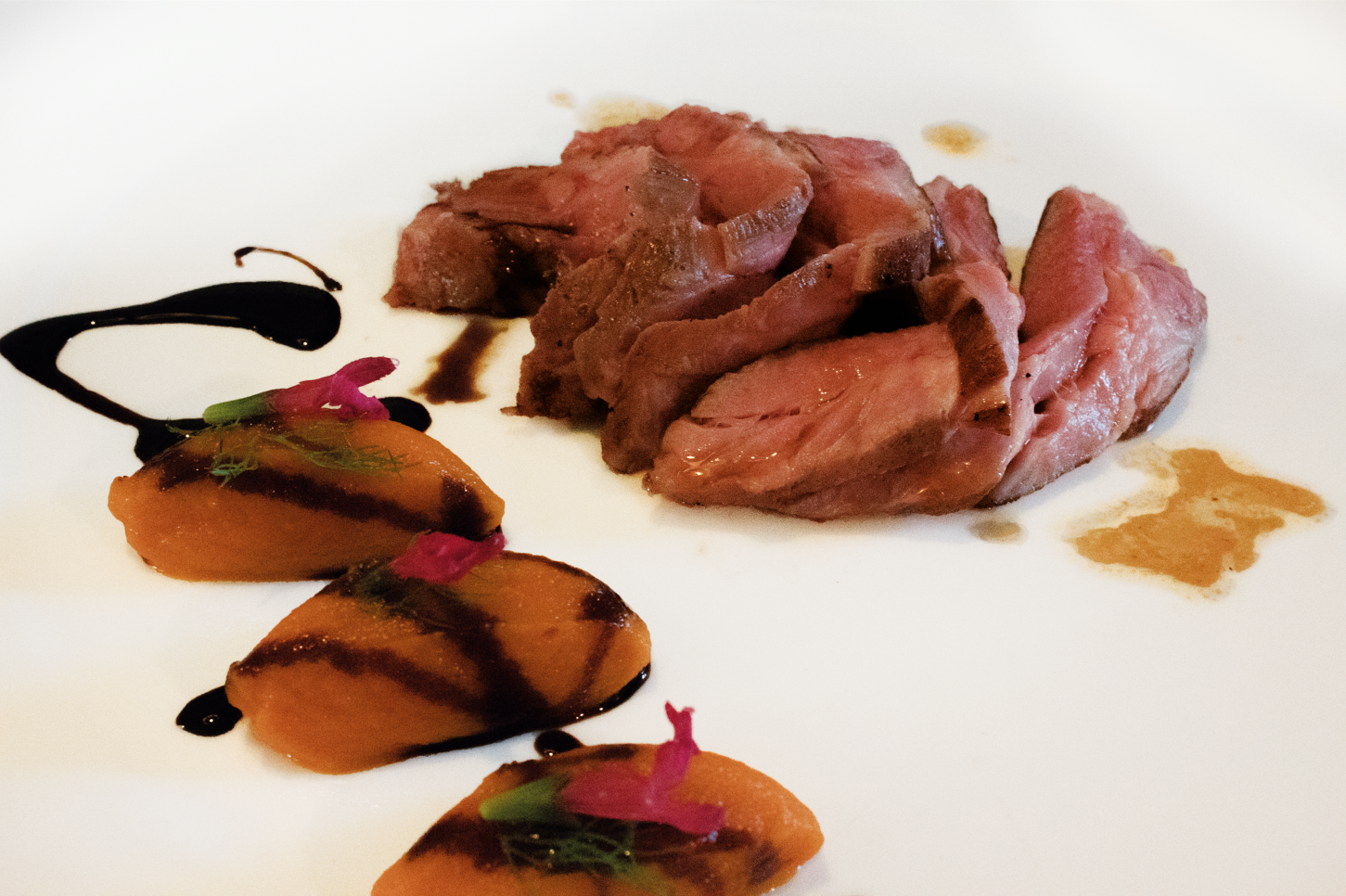 Carne affettata con salsa e verdure di contorno servita su un piatto bianco.