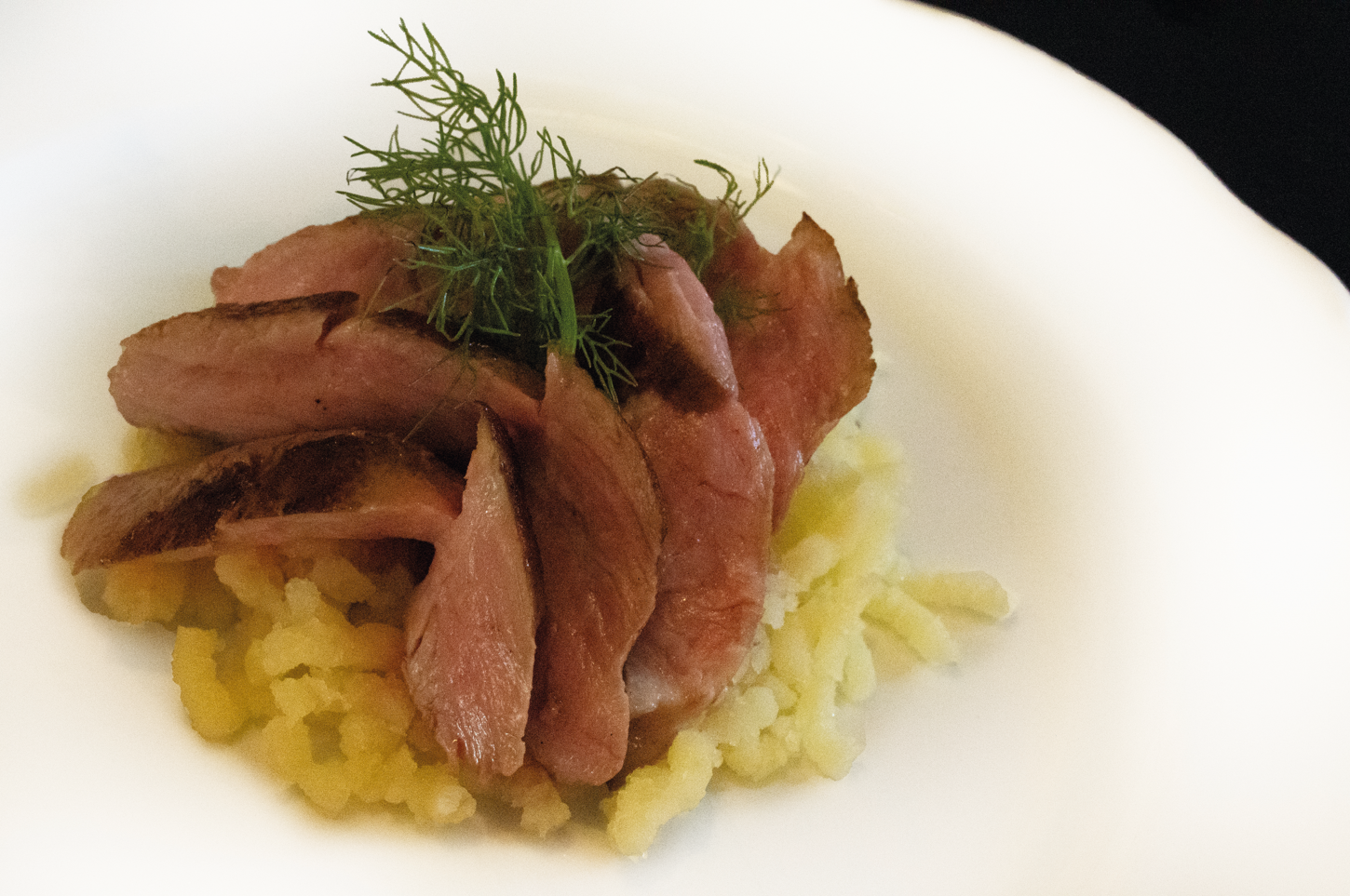 Carne affettata su un letto di purè di patate, guarnita con erbe aromatiche su un piatto bianco.