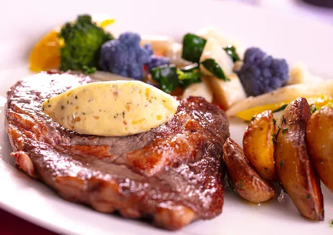Steak nappé de beurre aux herbes, servi avec des pommes de terre rôties et du brocoli sur une assiette blanche