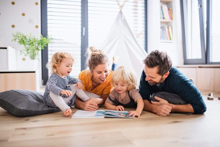 A family is laying on the floor reading a book together.