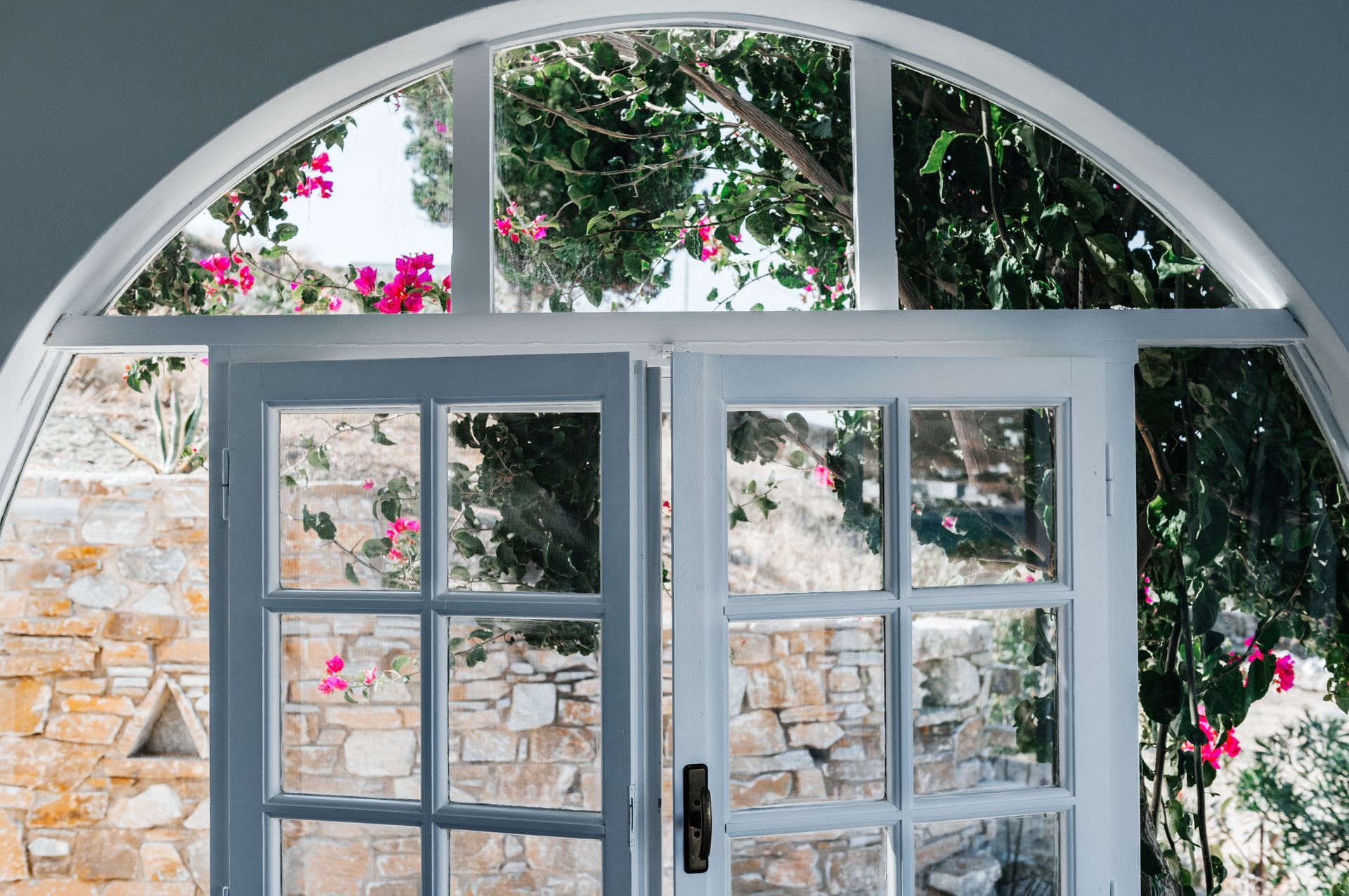 White arched doorway open to a stone patio with pink flowers.