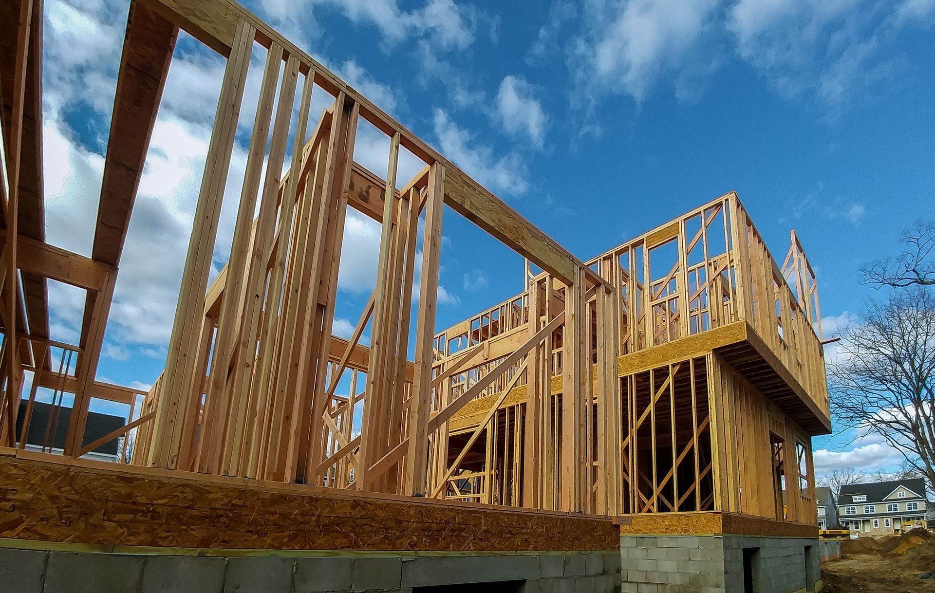 Wooden house under construction against a bright blue sky with scattered clouds.