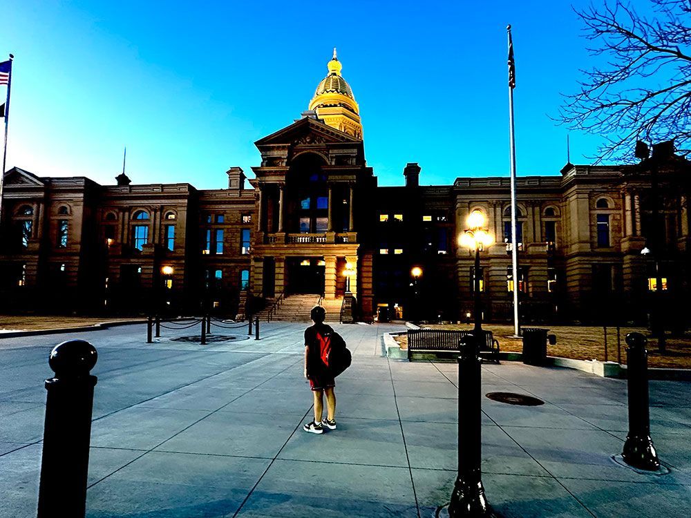 A person stands before a grand building with a golden dome at dusk.