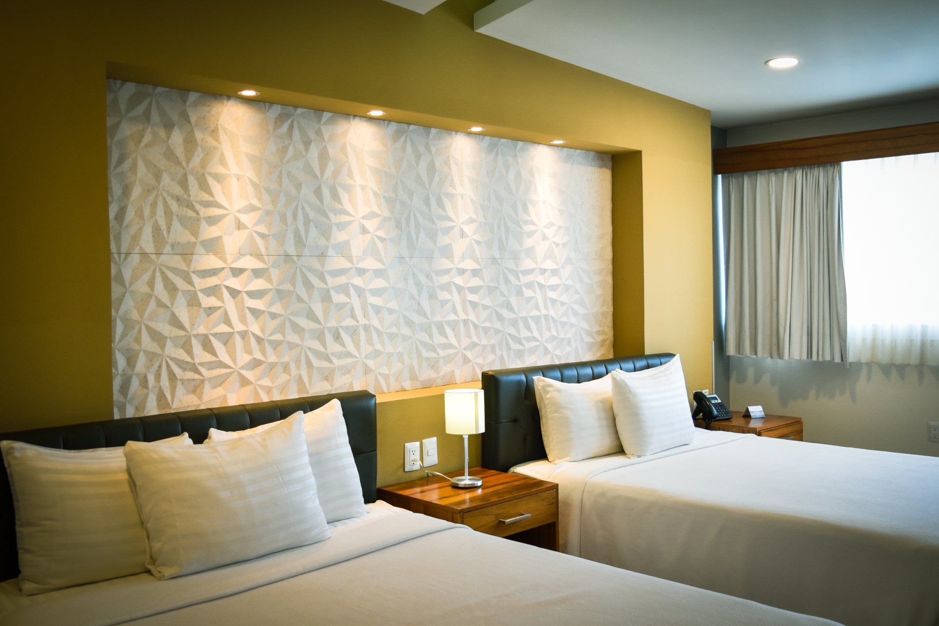 A hotel room with two beds , a nightstand and a window.