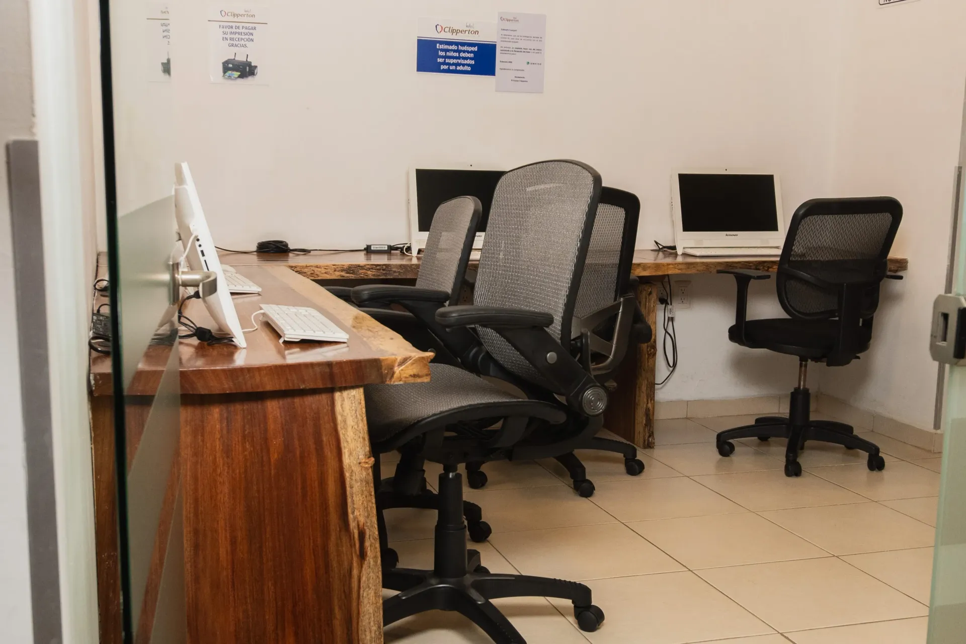Oficina con escritorios de madera, dos equipos informáticos y sillas giratorias de malla .