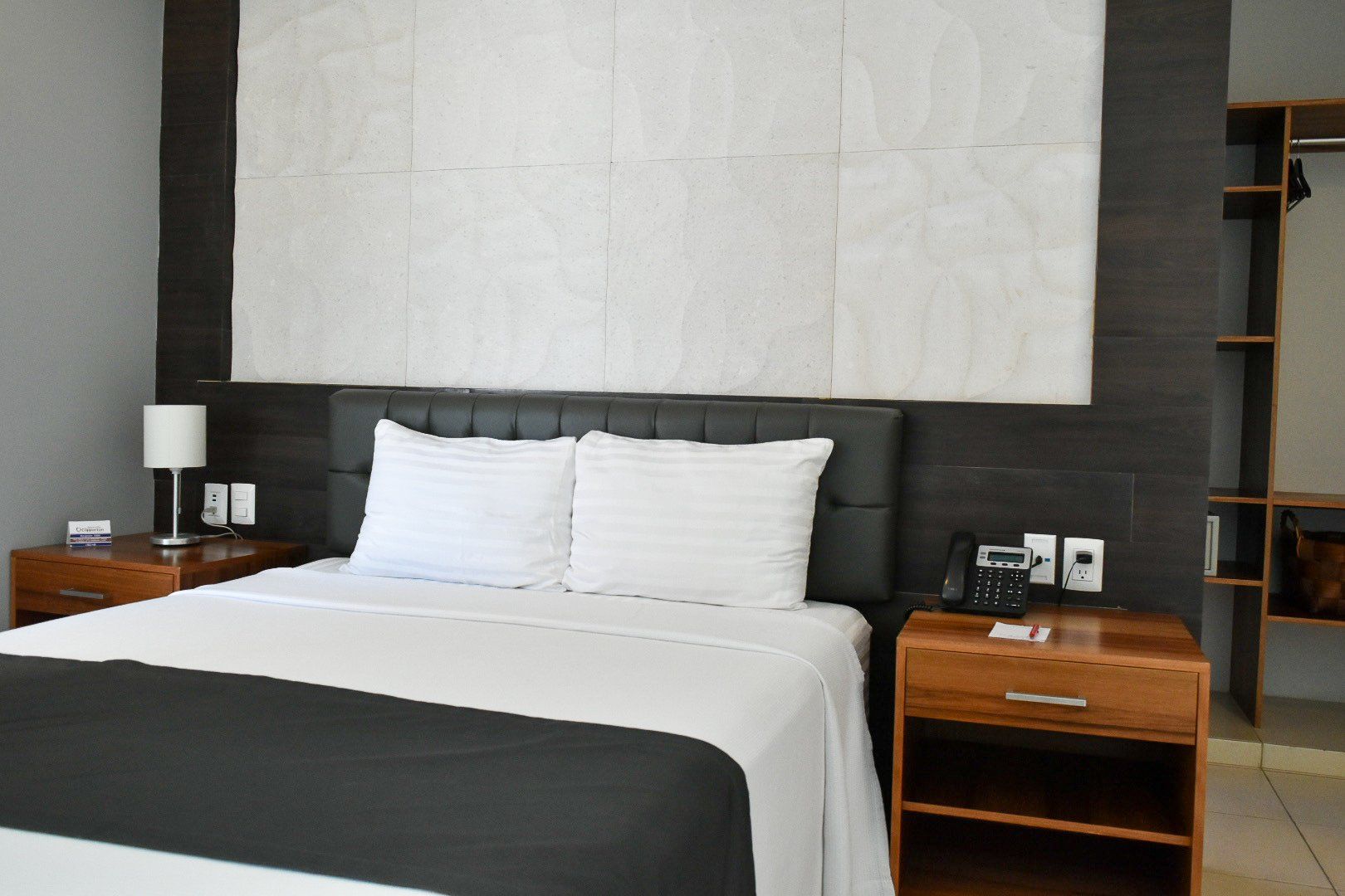 A hotel room with a bed , nightstand , lamp and telephone.