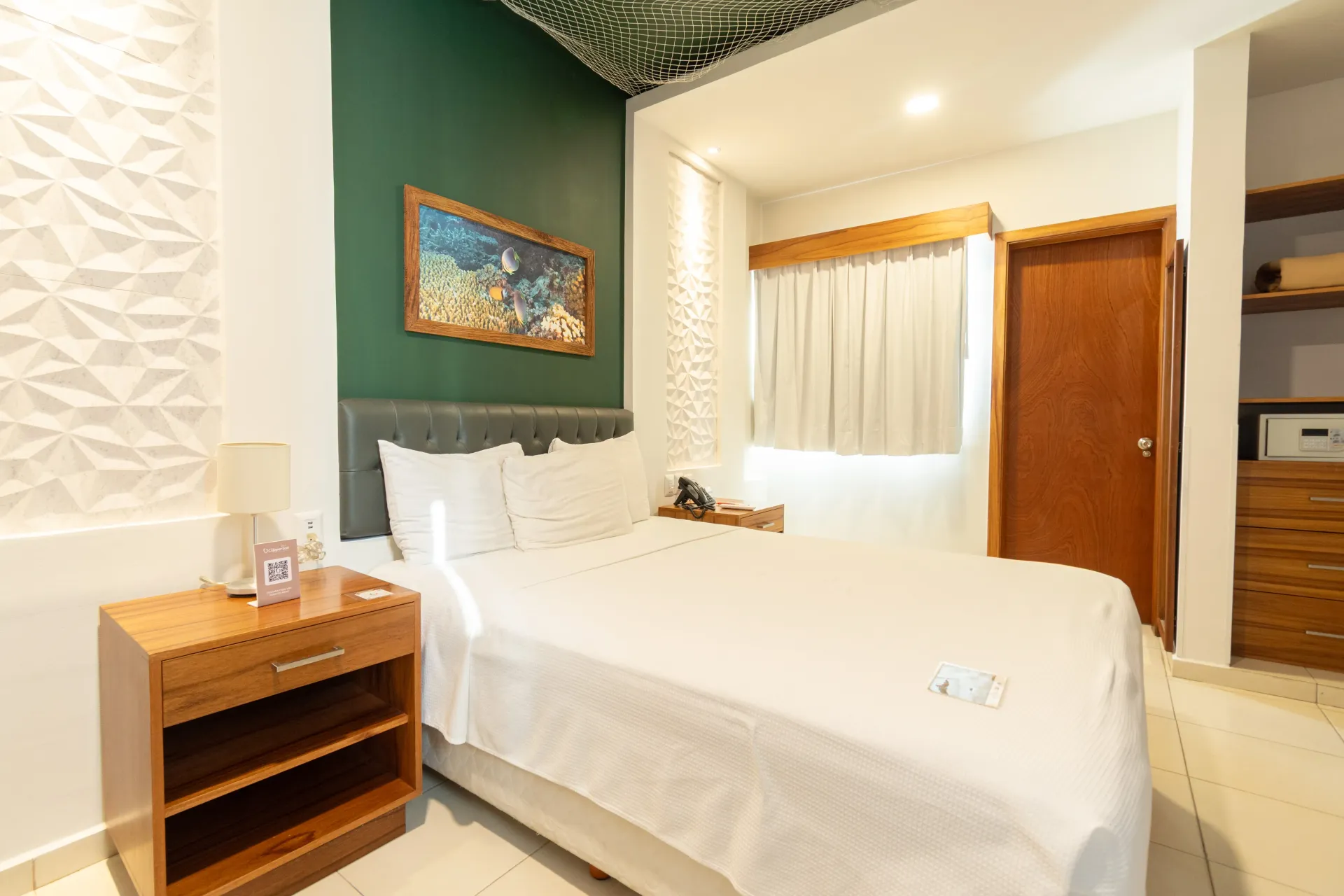 A clean, modern hotel room with a queen bed, green accent wall, textured white wall, wood nightstand, and closet.