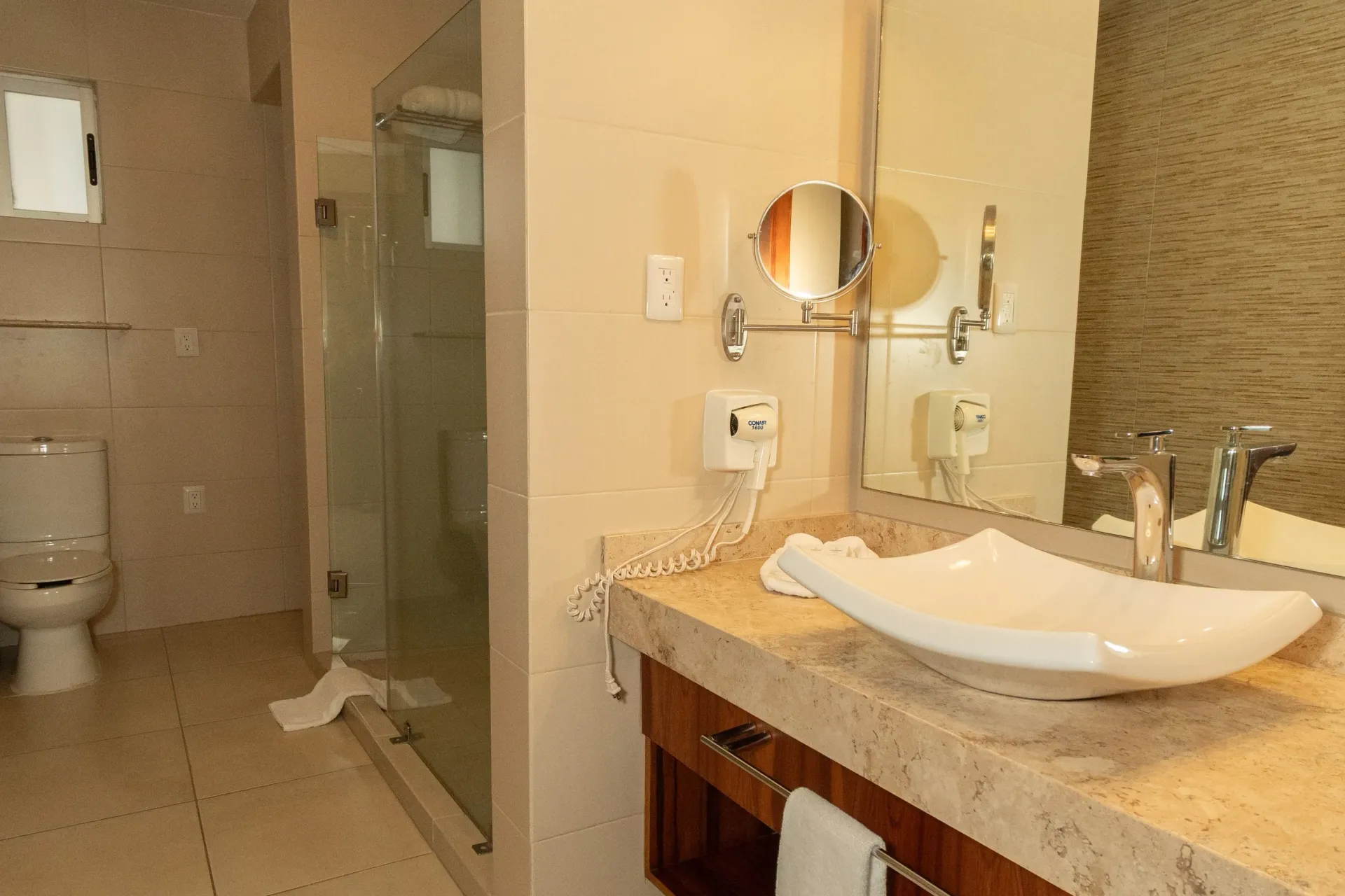A bathroom featuring a beige stone countertop, a modern white vessel sink, a mounted mirror, and a glass-enclosed shower.