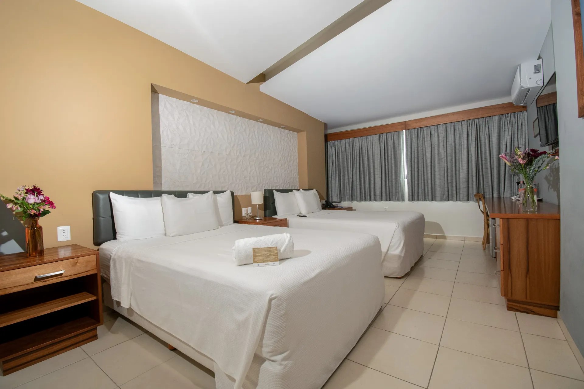 Una habitación de hotel con dos camas, una mesita de noche y una ventana.
