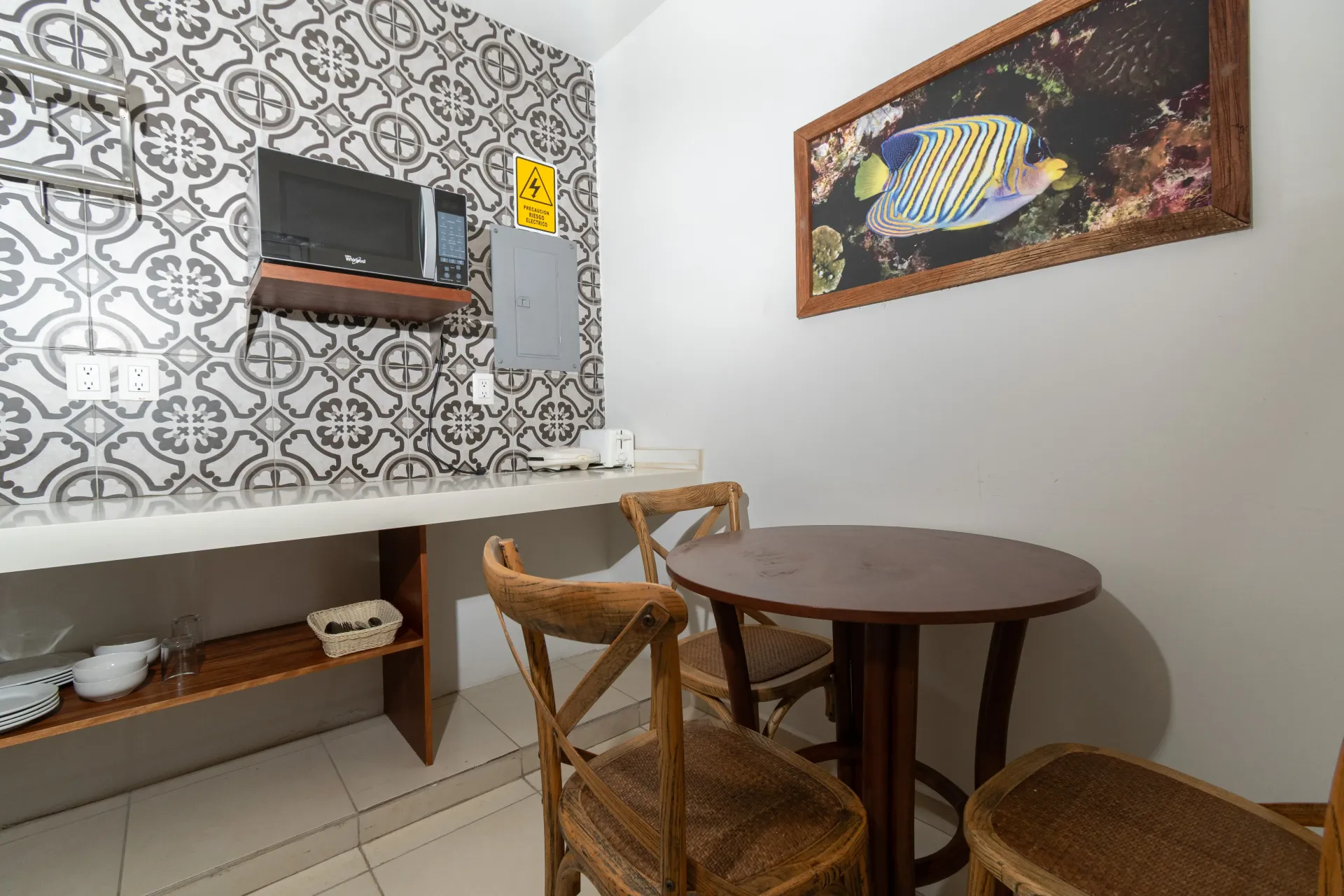 A small dining area with a round wooden table, two wooden chairs, and a kitchen counter with a microwave.