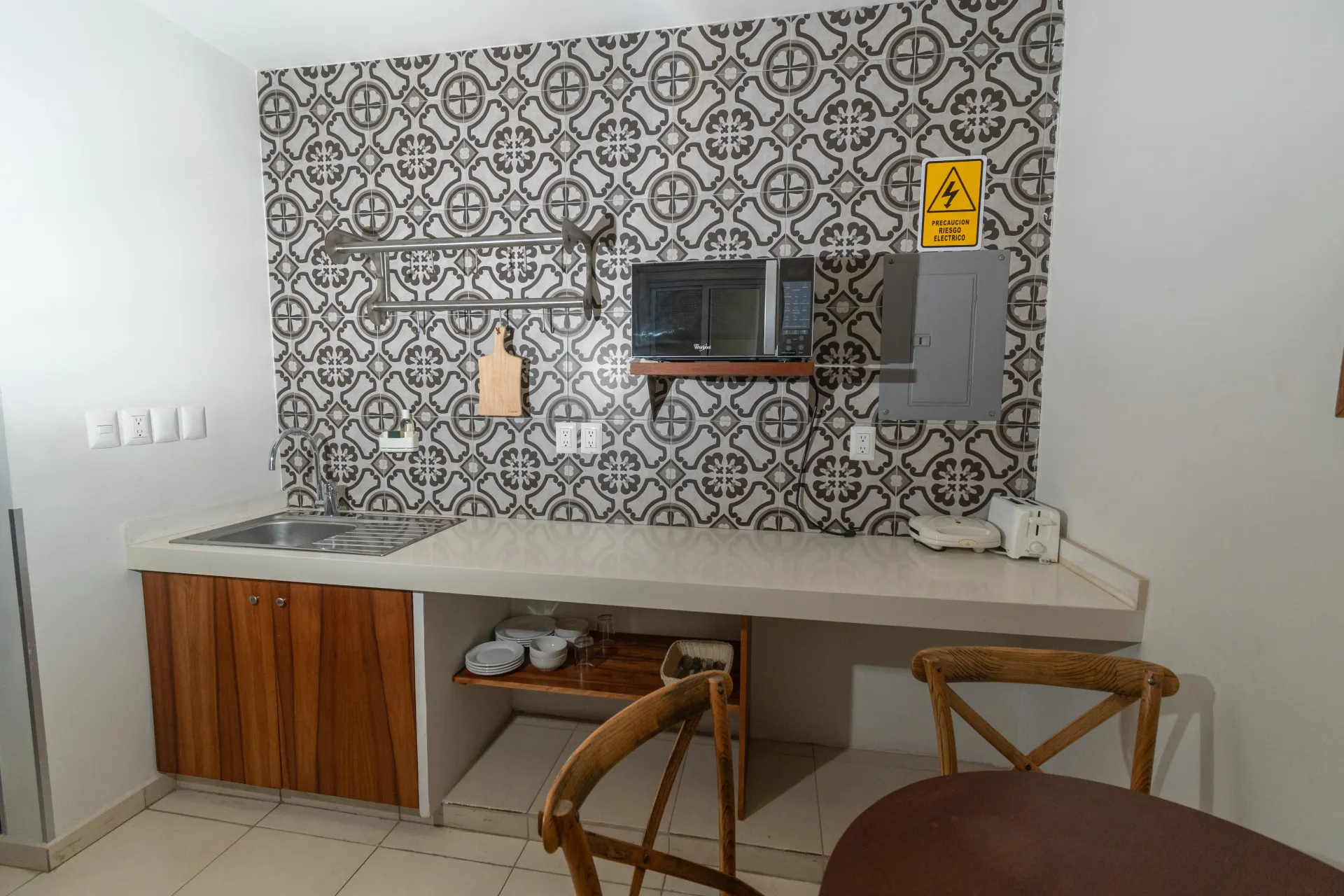 A small kitchen area with a patterned tiled backsplash, a microwave, a wooden cabinet, and a dining table with chairs.
