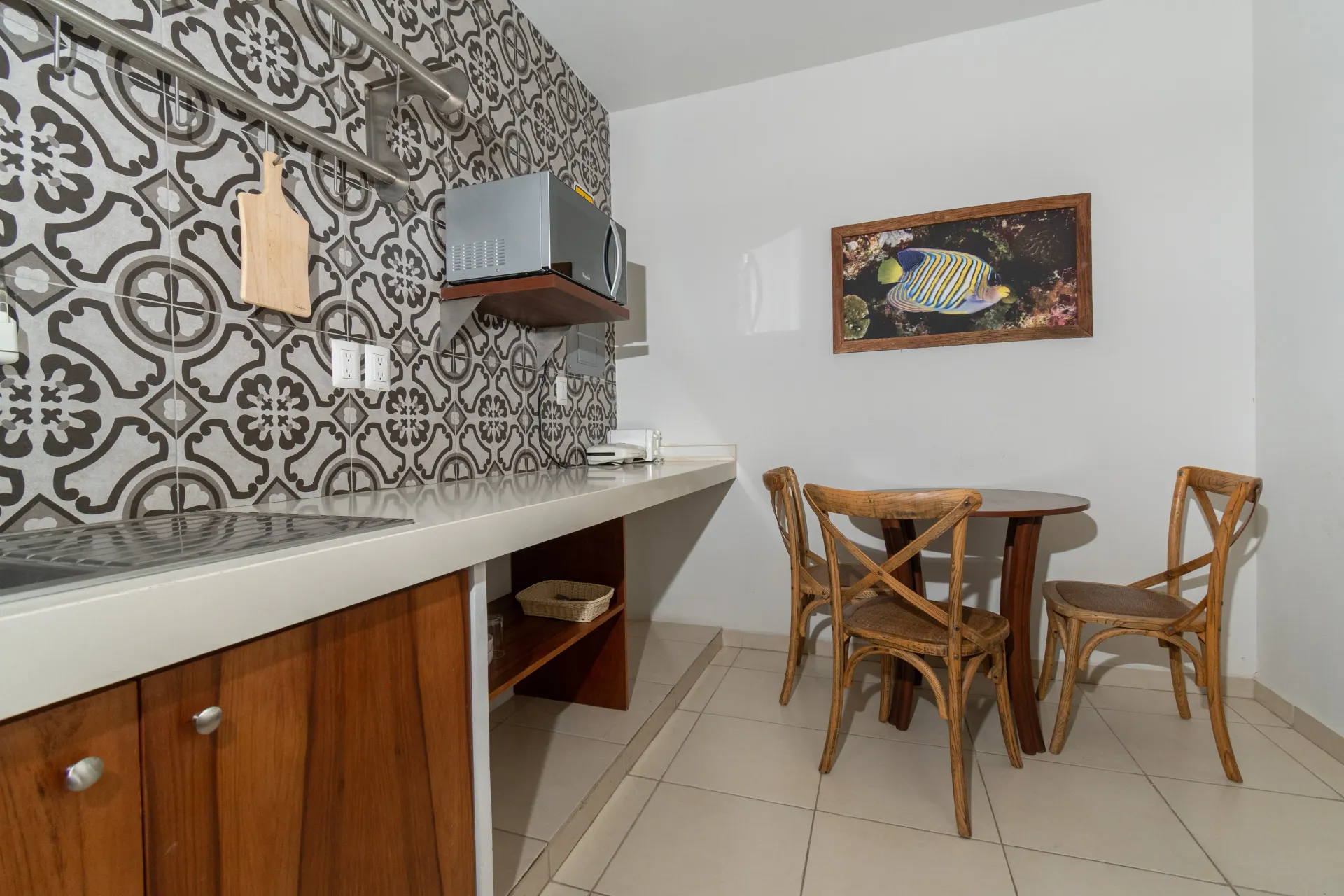 A small kitchen with patterned tile walls, a wooden counter, a microwave, and a dining table with two wicker chairs.