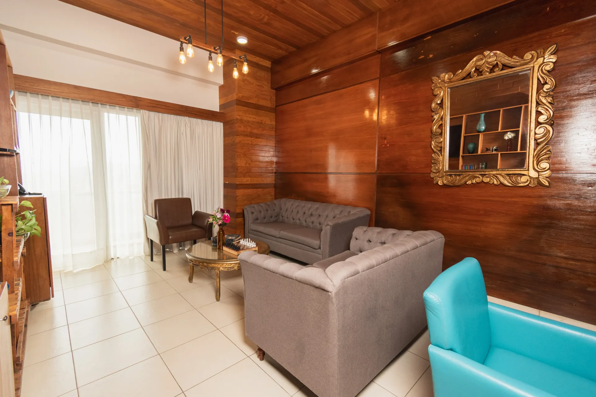 USala de estar con paredes y estanterías de madera, TV, dos sofás grises, un sillón marrón y una silla color turquesa.