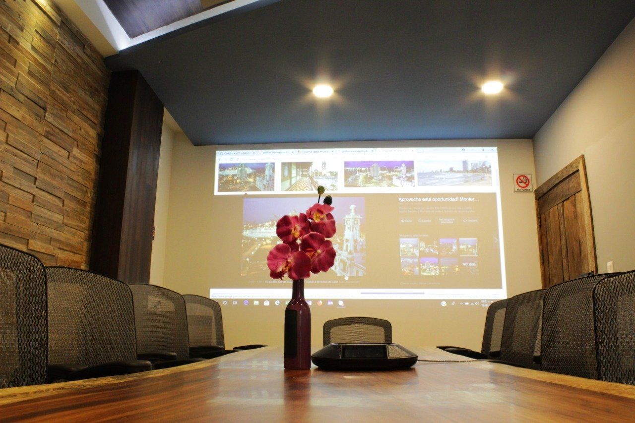 Una sala de conferencias con una pantalla de proyector y un jarrón de flores sobre la mesa.
