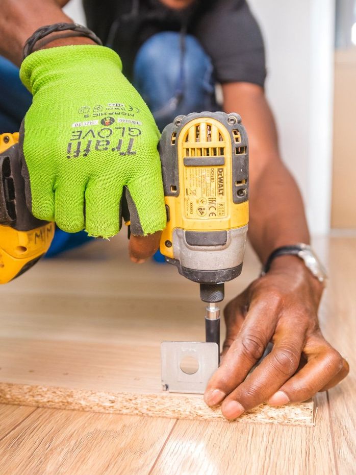 A person using a Dewalt screw gun to place a screw into a cupboard door