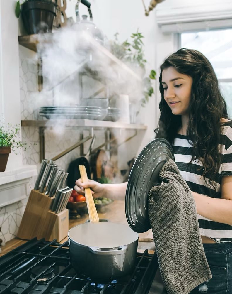 Woman stirring steaming food in a pot on a kitchen stove