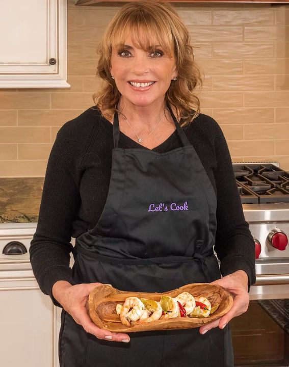 Woman in a kitchen holding a platter of sliced bread topped with cheese and herbs.