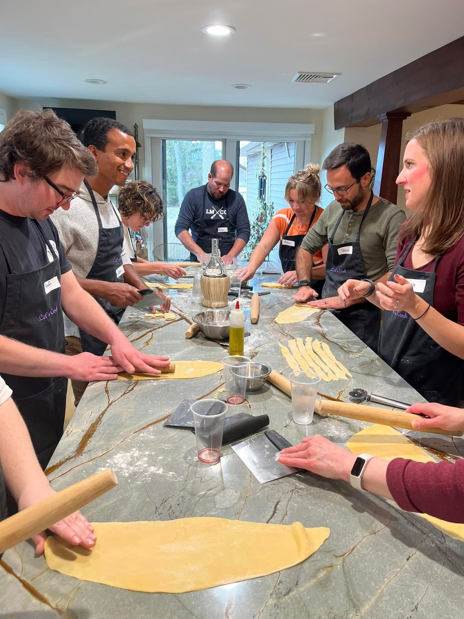 People rolling pasta dough around a kitchen island, sharing a cooking lesson