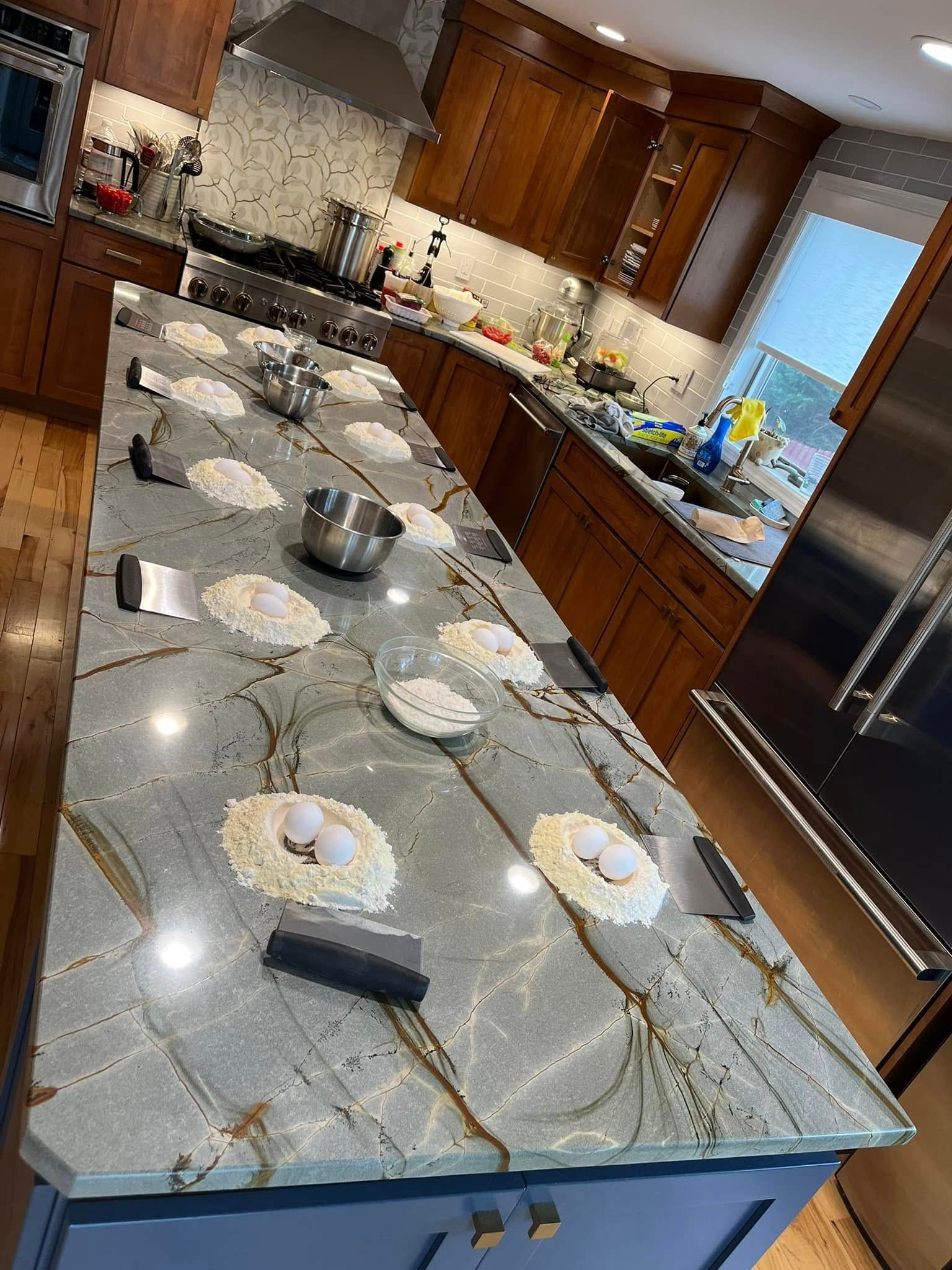 Modern kitchen with marble island, plates set out, and wooden cabinets; granite countertop with dishes and bowls.