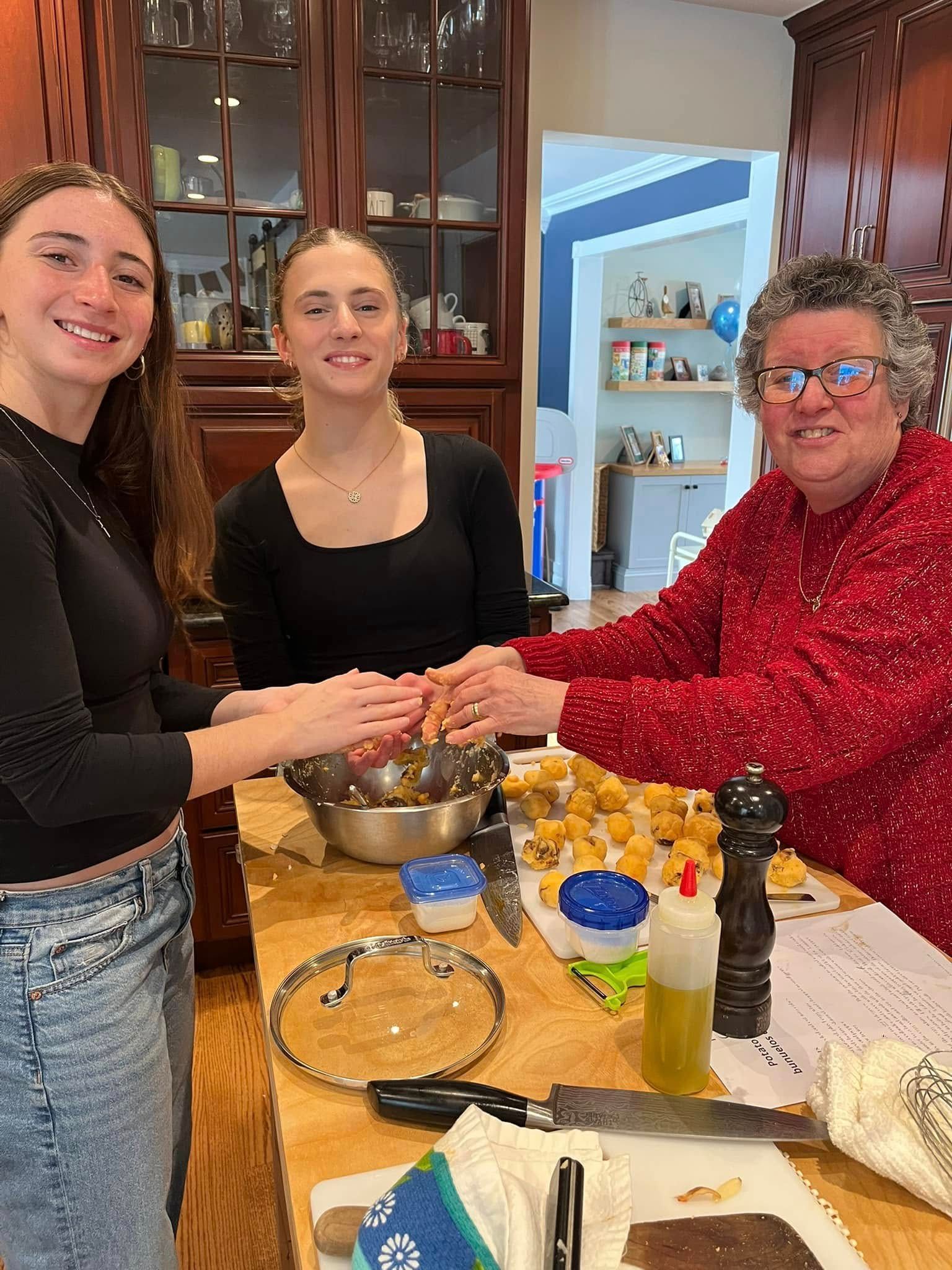 Three people mixing ingredients at a kitchen counter, with bowls, fruit, and baking supplies.