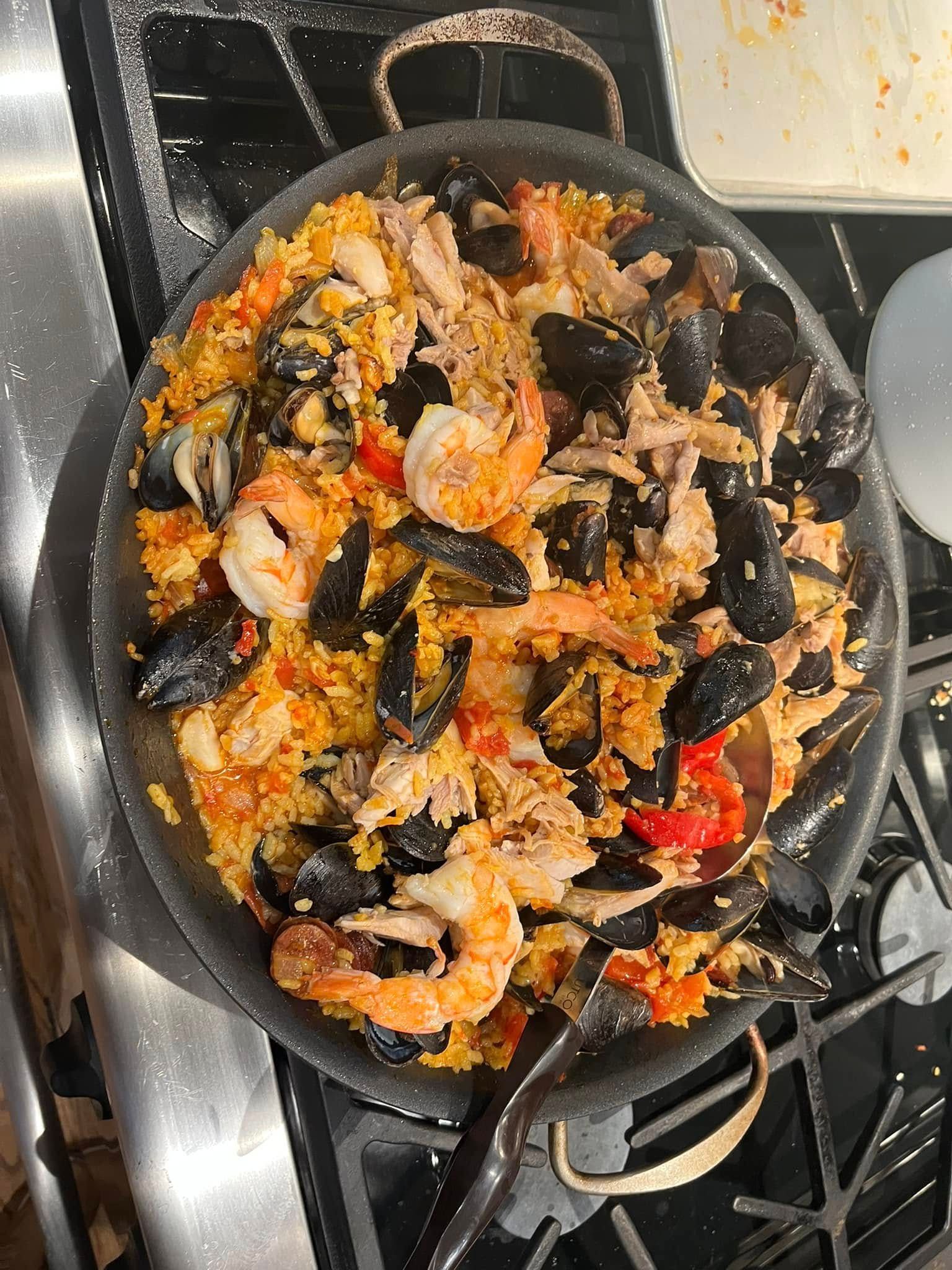 Pan of shrimp and mussels mixed with rice and red peppers on a stovetop