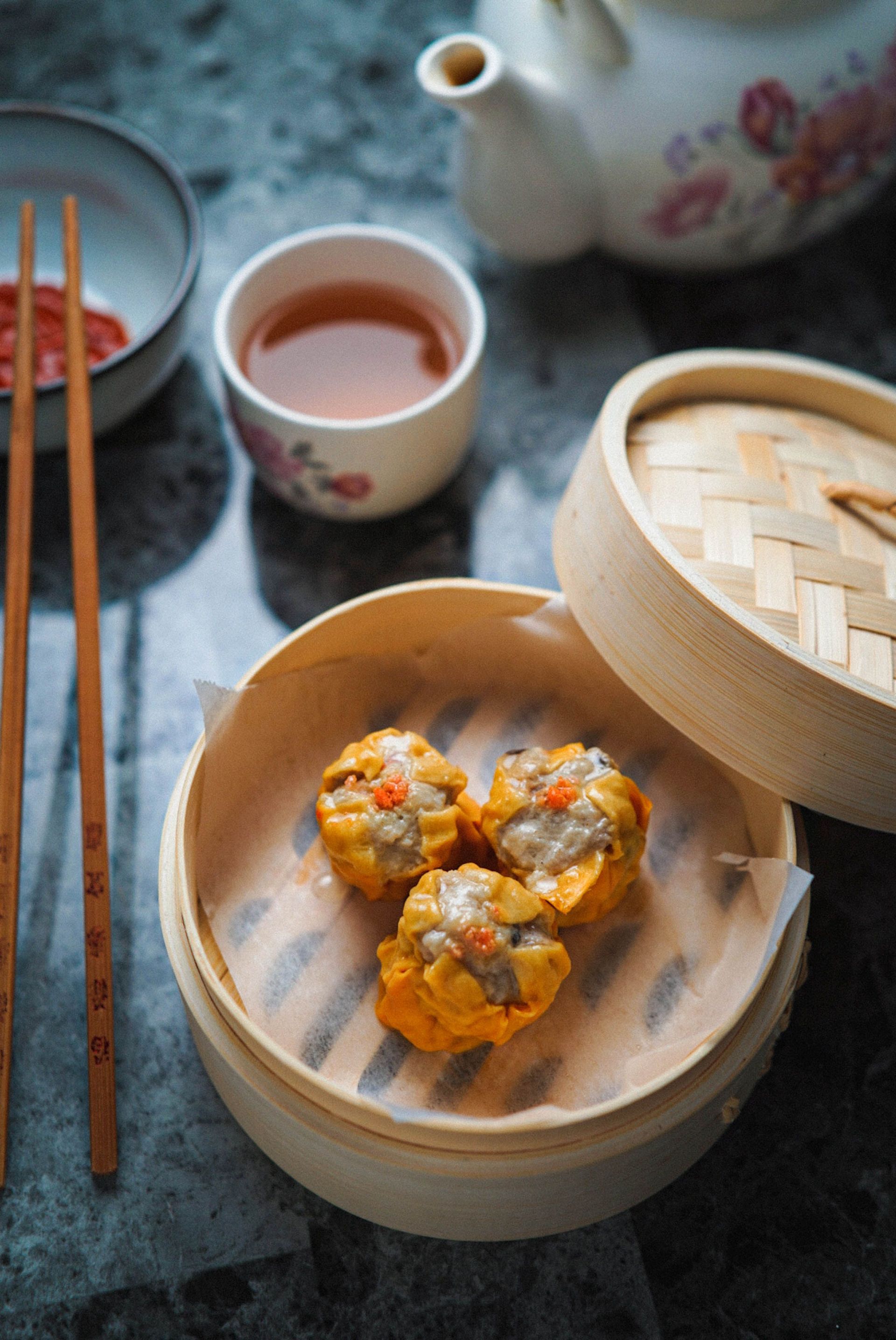 Steamed dim sum in a bamboo basket with tea on a table