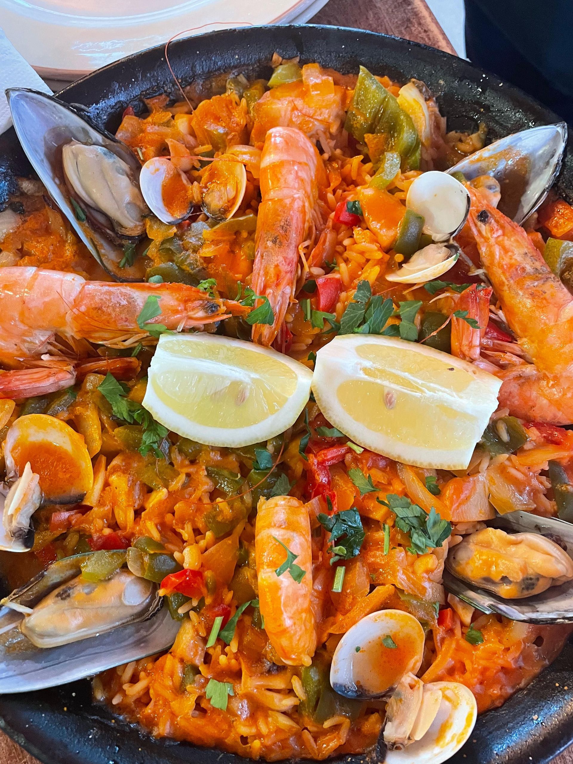 Seafood paella in a black pan, topped with mussels, shrimp, and lemon wedges