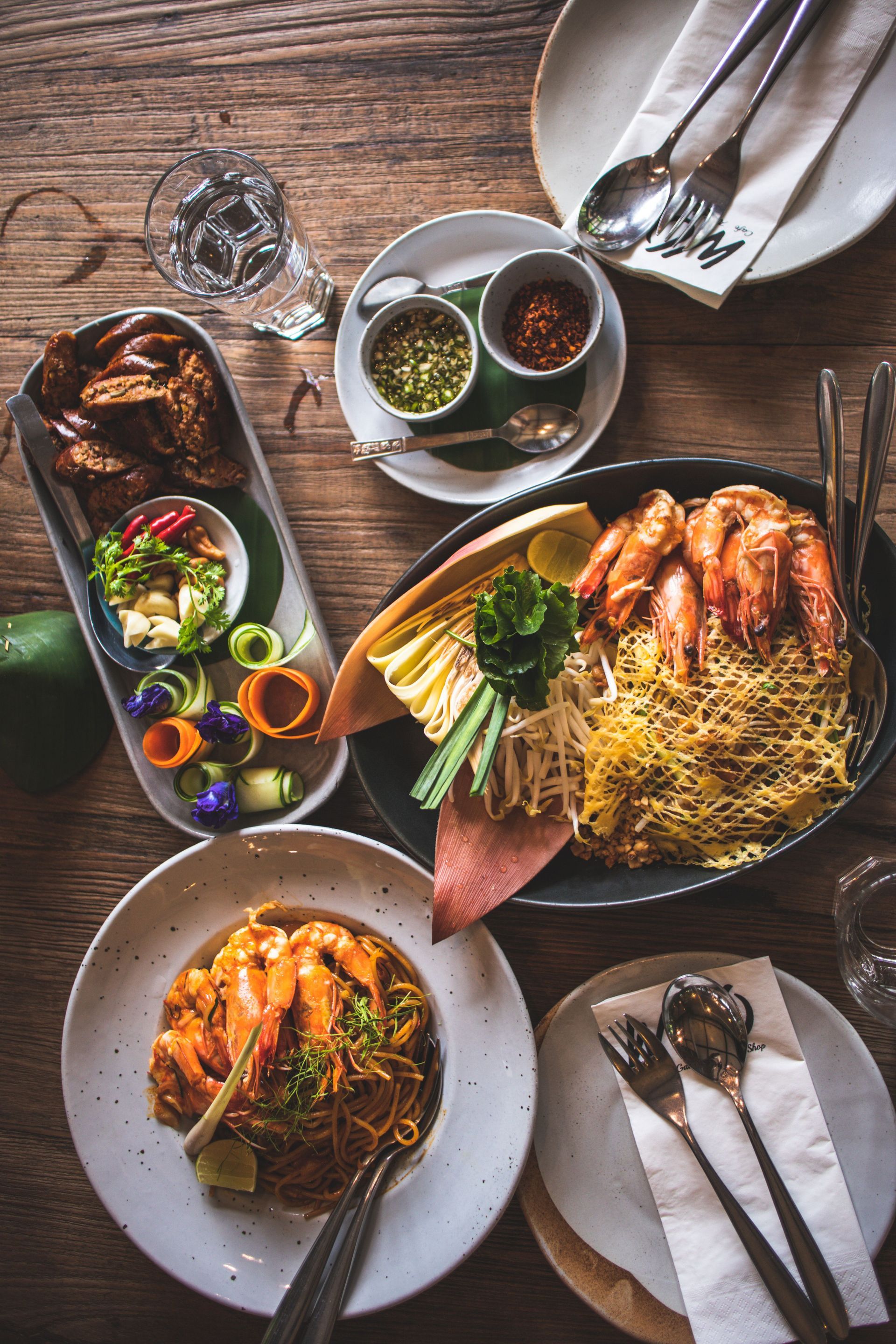 Overhead view of a table with assorted plated dishes, salads, and condiments on wooden tabletop