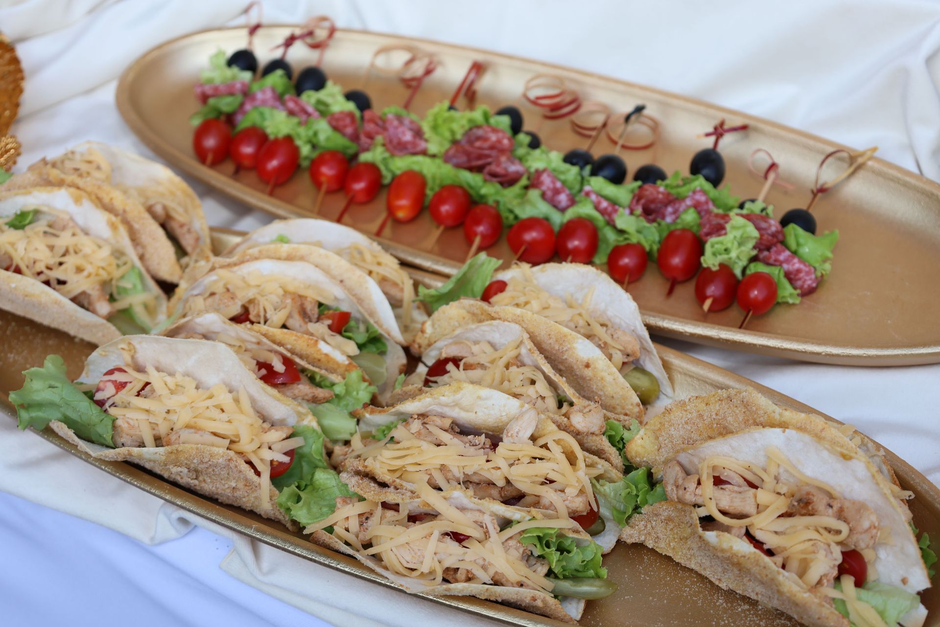 Platter of rolled sandwiches and cherry tomato skewers on white tablecloth, garnished with herbs