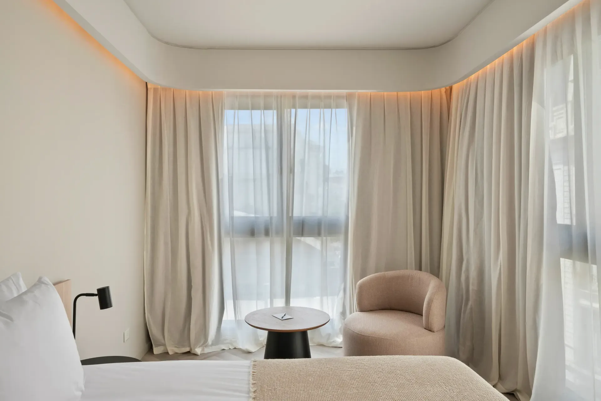 Una habitación de hotel con una cama, una silla, una mesa y cortinas.