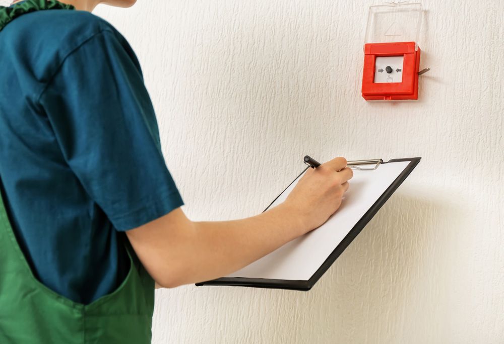 Focused Individual Inspecting a Red Fire Alarm, Diligently Noting Details on a Clipboard - Dubbo NSW