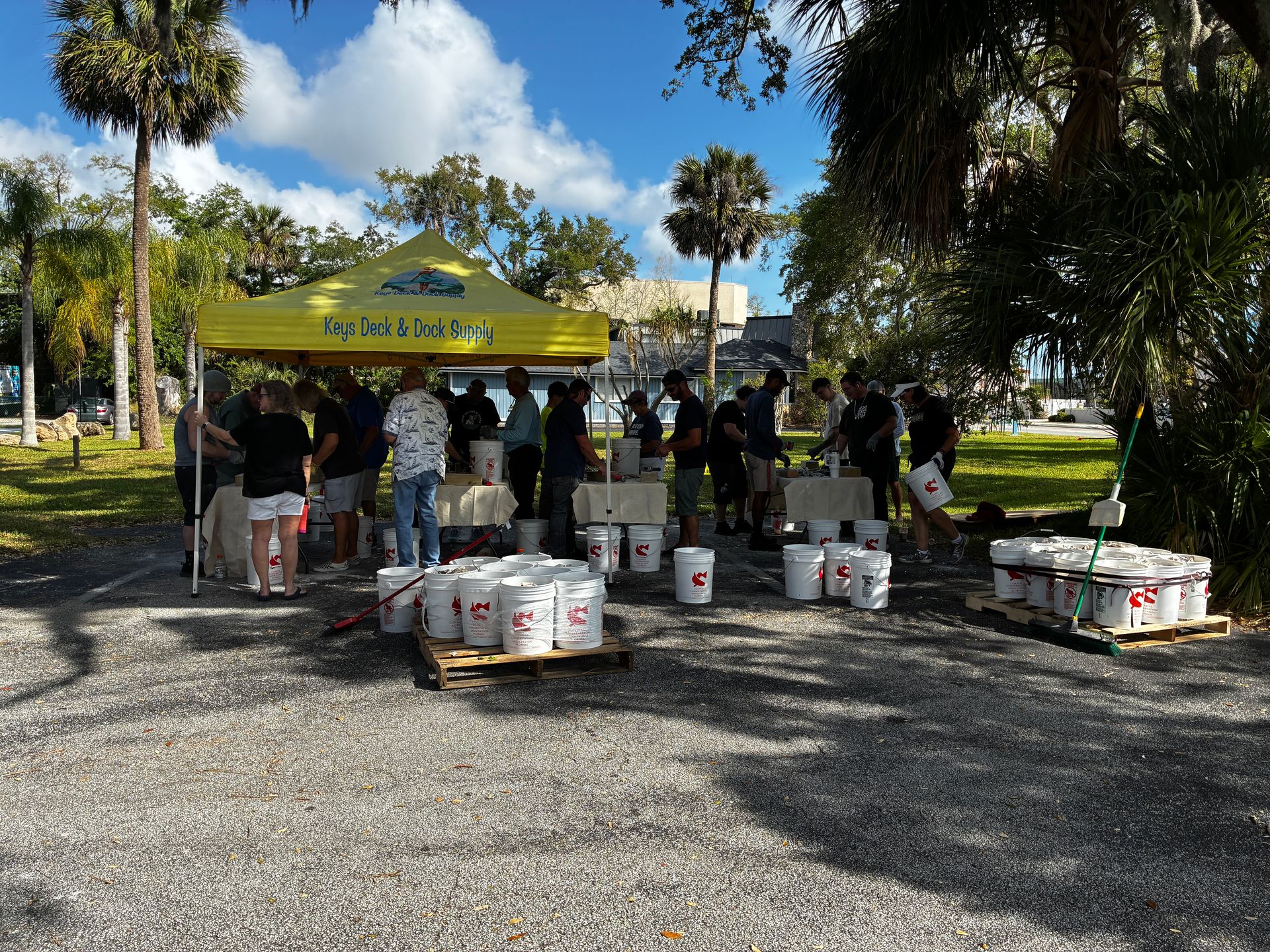 Volunteers under a yellow tent handing out supplies in a sunny park, with boxes and coolers on the ground.