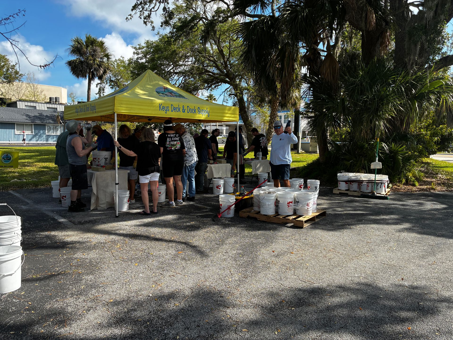 People under a yellow canopy serving food at an outdoor event, with tables and palm trees nearby