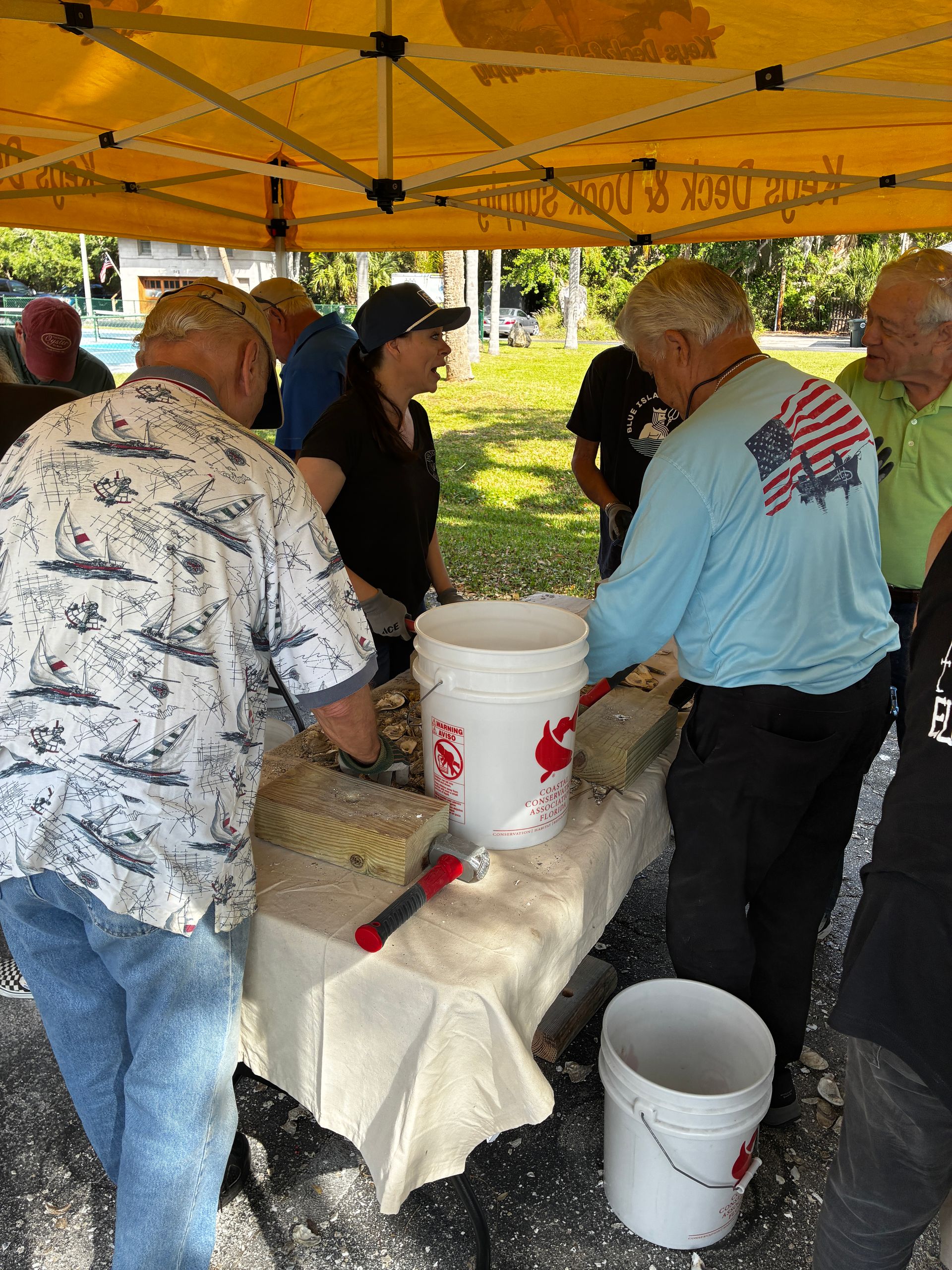 People serving food at an outdoor picnic table under a yellow canopy