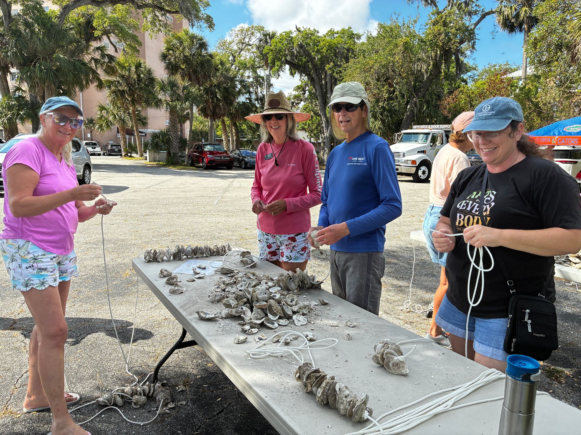 People at an outdoor table sorting shells or rocks in a sunny park area