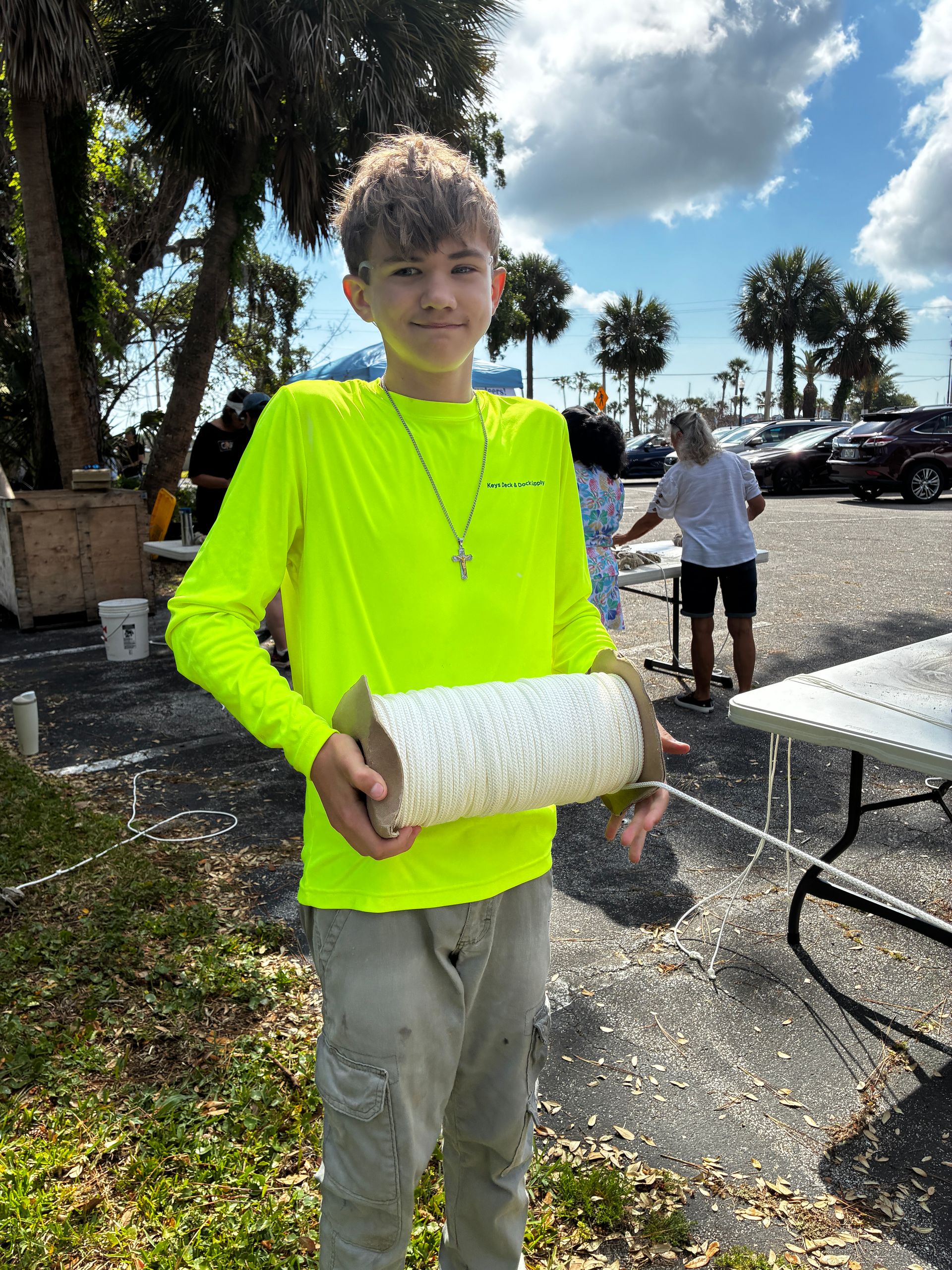 Person in a neon yellow shirt holding a white rolled mat outdoors on a sunny day.
