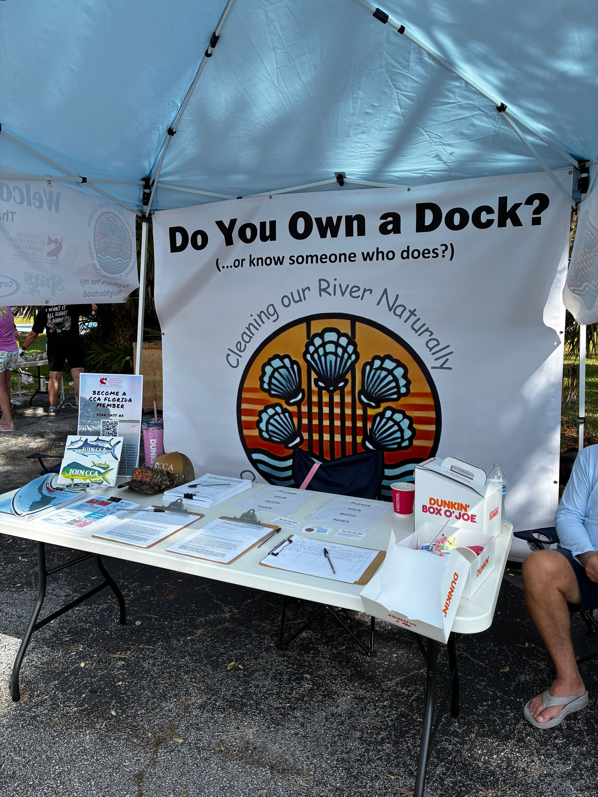 Booth under canopy with “Do You Own a Dock?” banner, brochures, and a seated person at a table