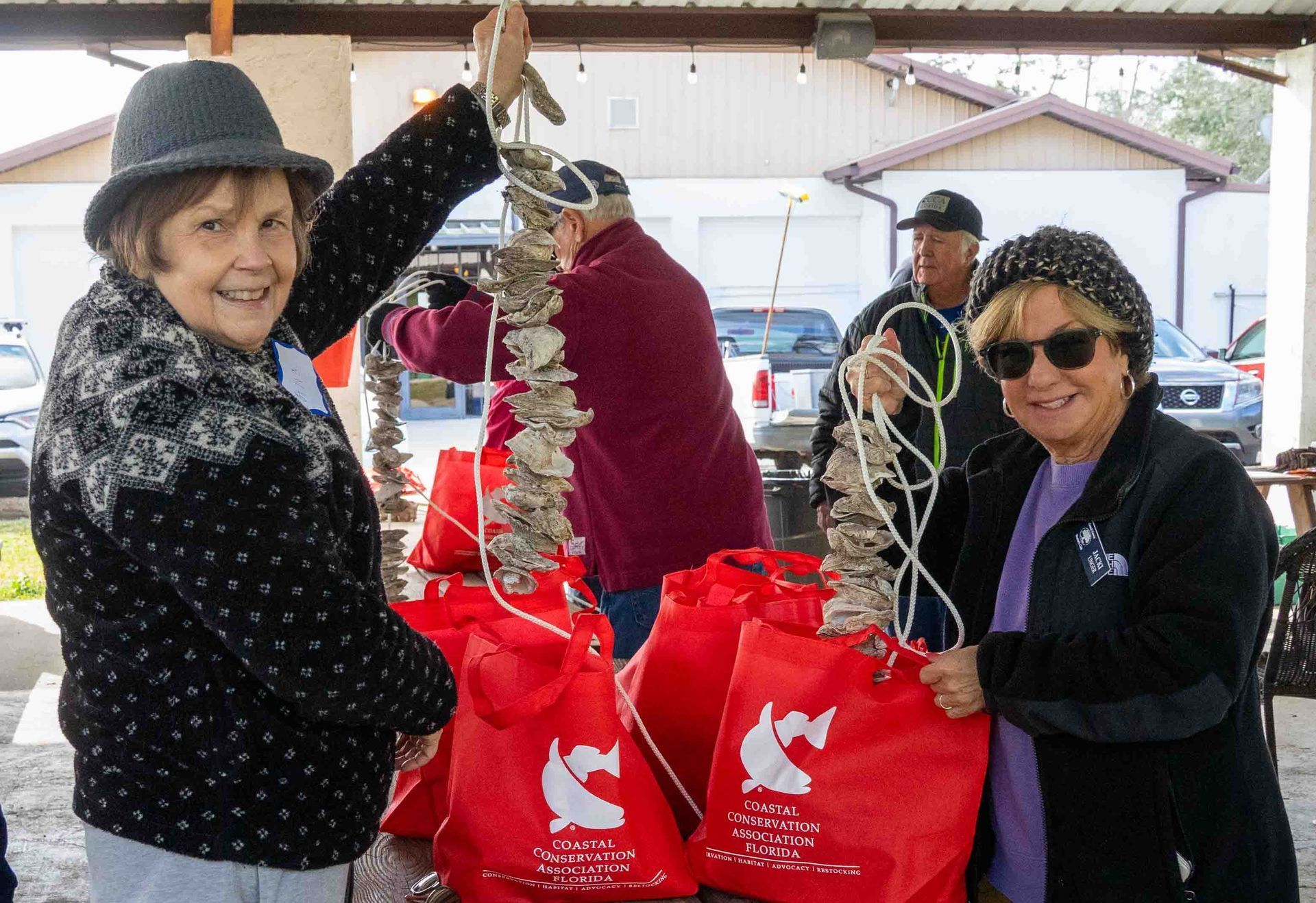 Volunteers holding red donation bags and holiday decor at an outdoor event under a tent