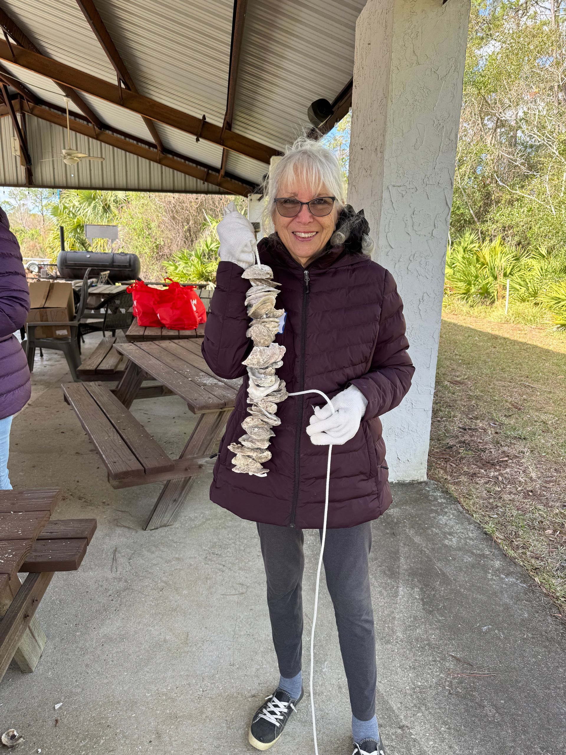 Woman in purple jacket holding a white floral lei in a picnic shelter, smiling at the camera.