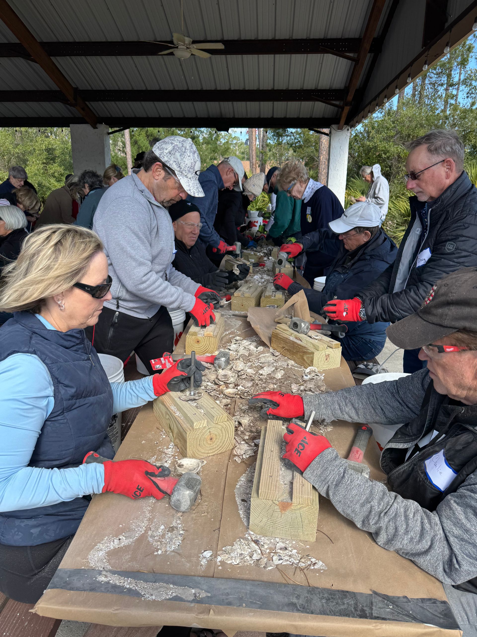 People carving a large log at an outdoor pavilion, wearing red gloves and winter jackets