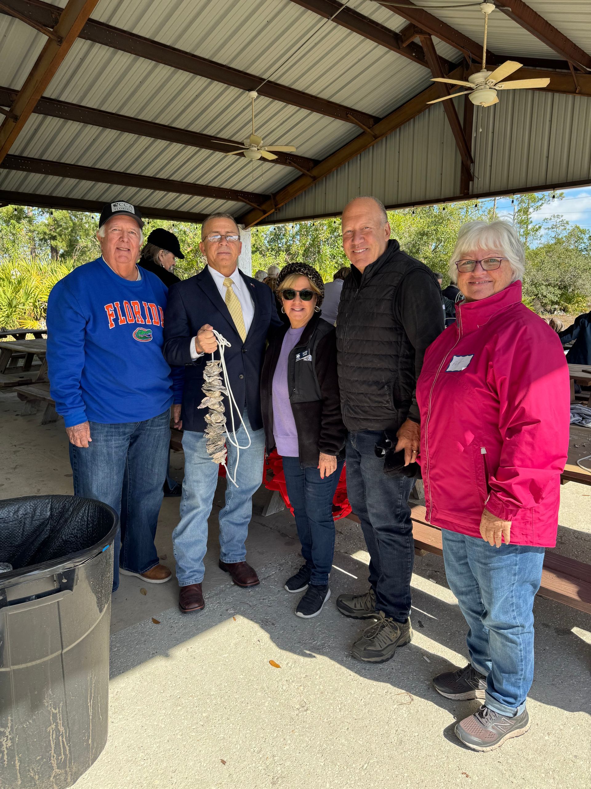 Five people standing together under a pavilion, smiling in winter jackets on a sunny day