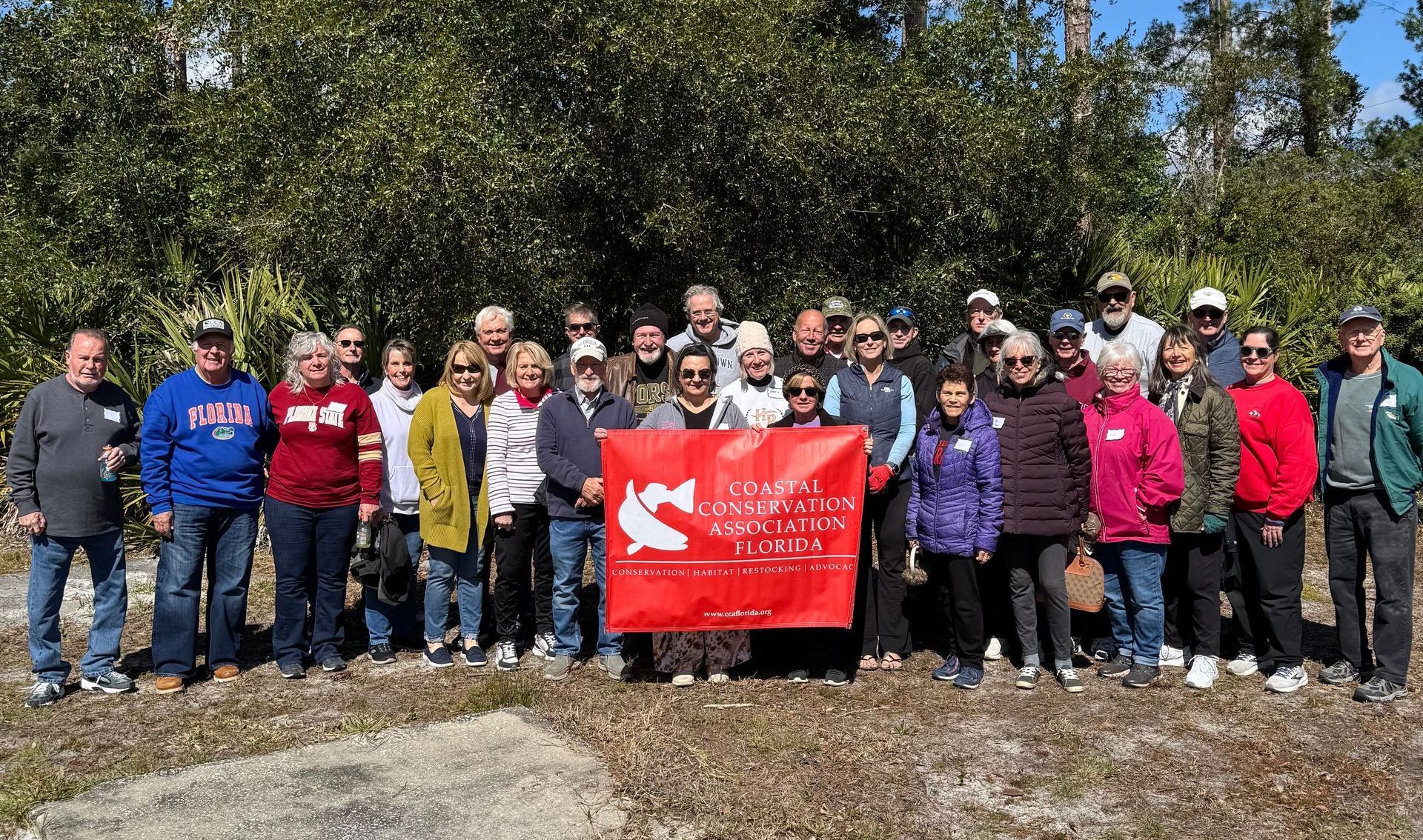 Group of people outdoors holding a red banner in front of trees on a sunny day
