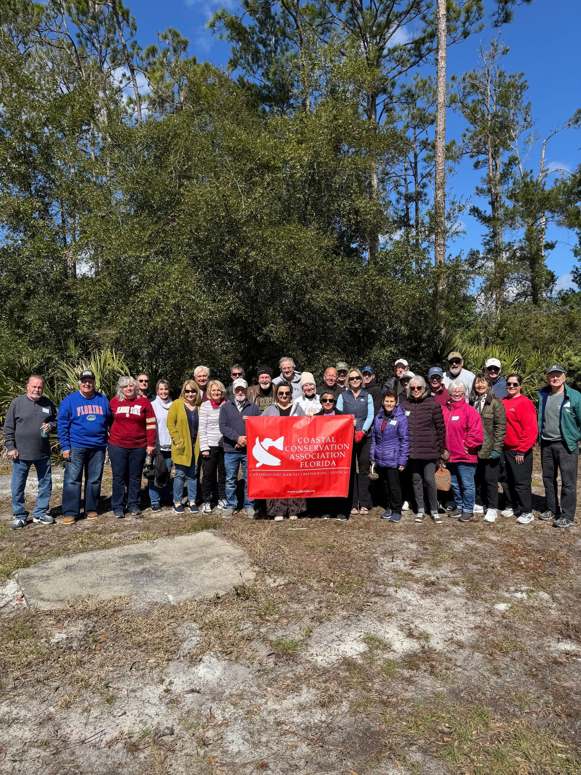Group of people outdoors holding a red banner in a wooded area under a blue sky