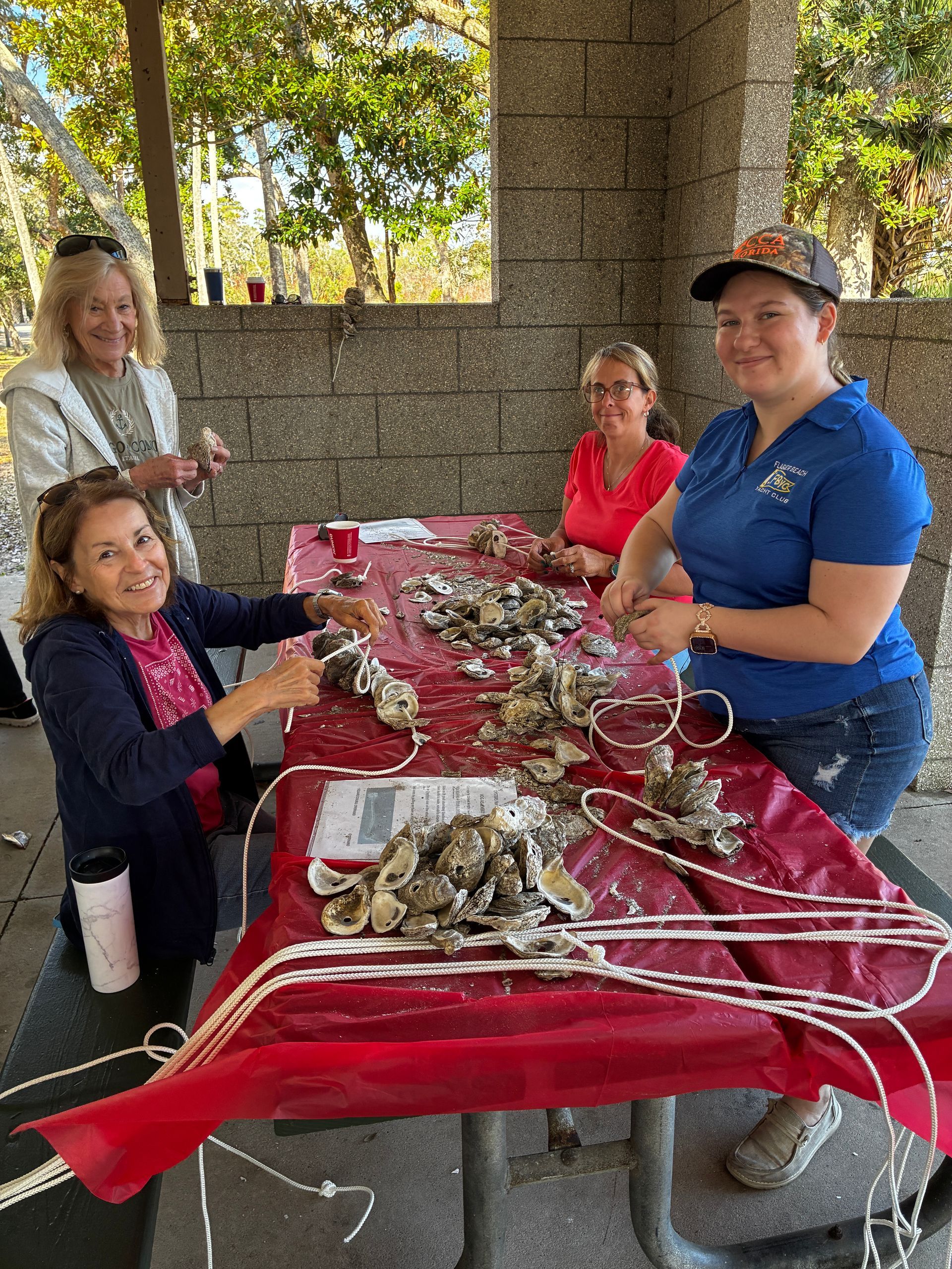 People seated at a picnic table crafting with branches and ribbons under a pavilion outdoors