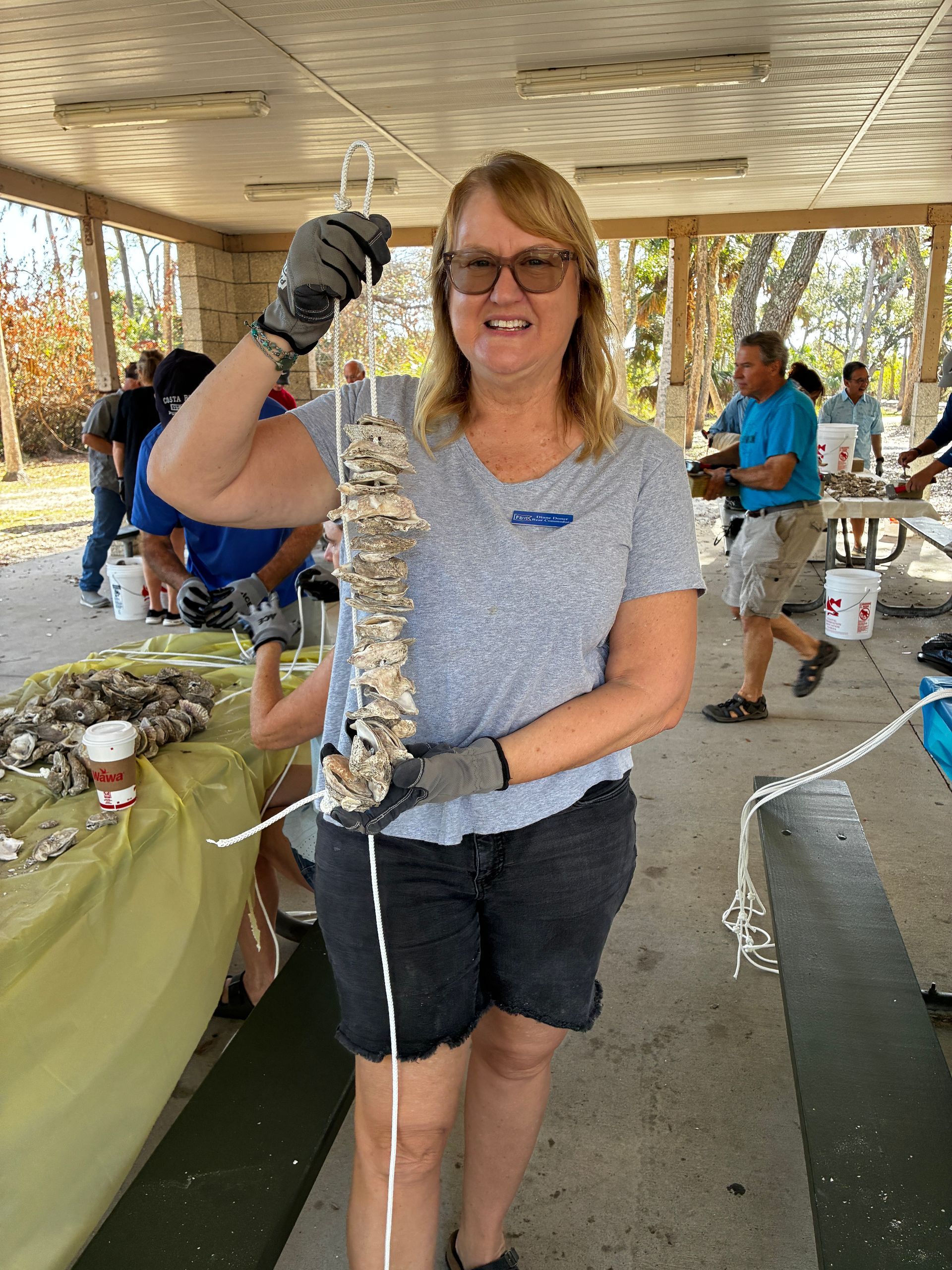 Woman holding a long fish at an outdoor pavilion, smiling beside a fish-cleaning table.