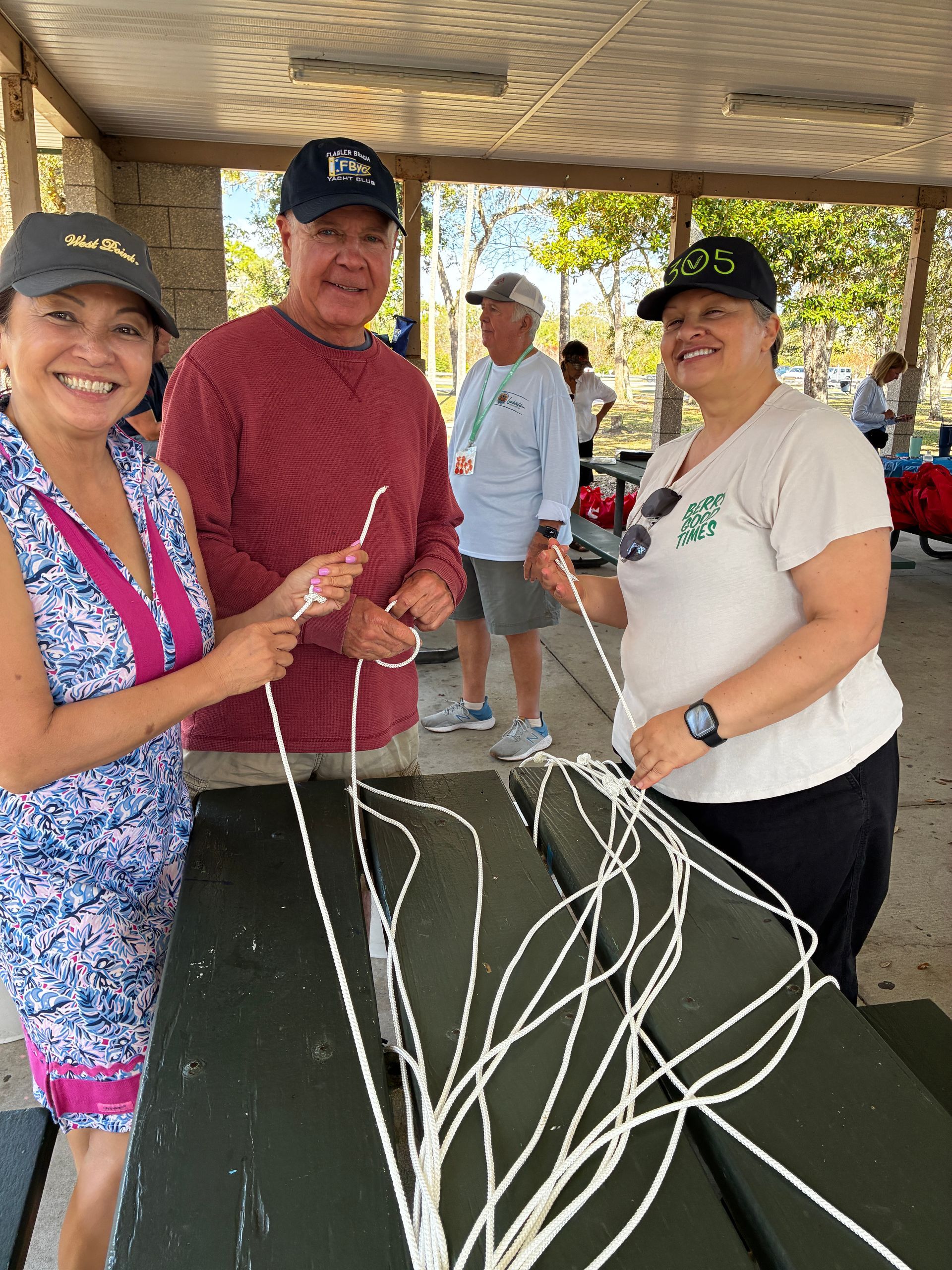 Three people smiling under a pavilion, holding fishing lines at a table display
