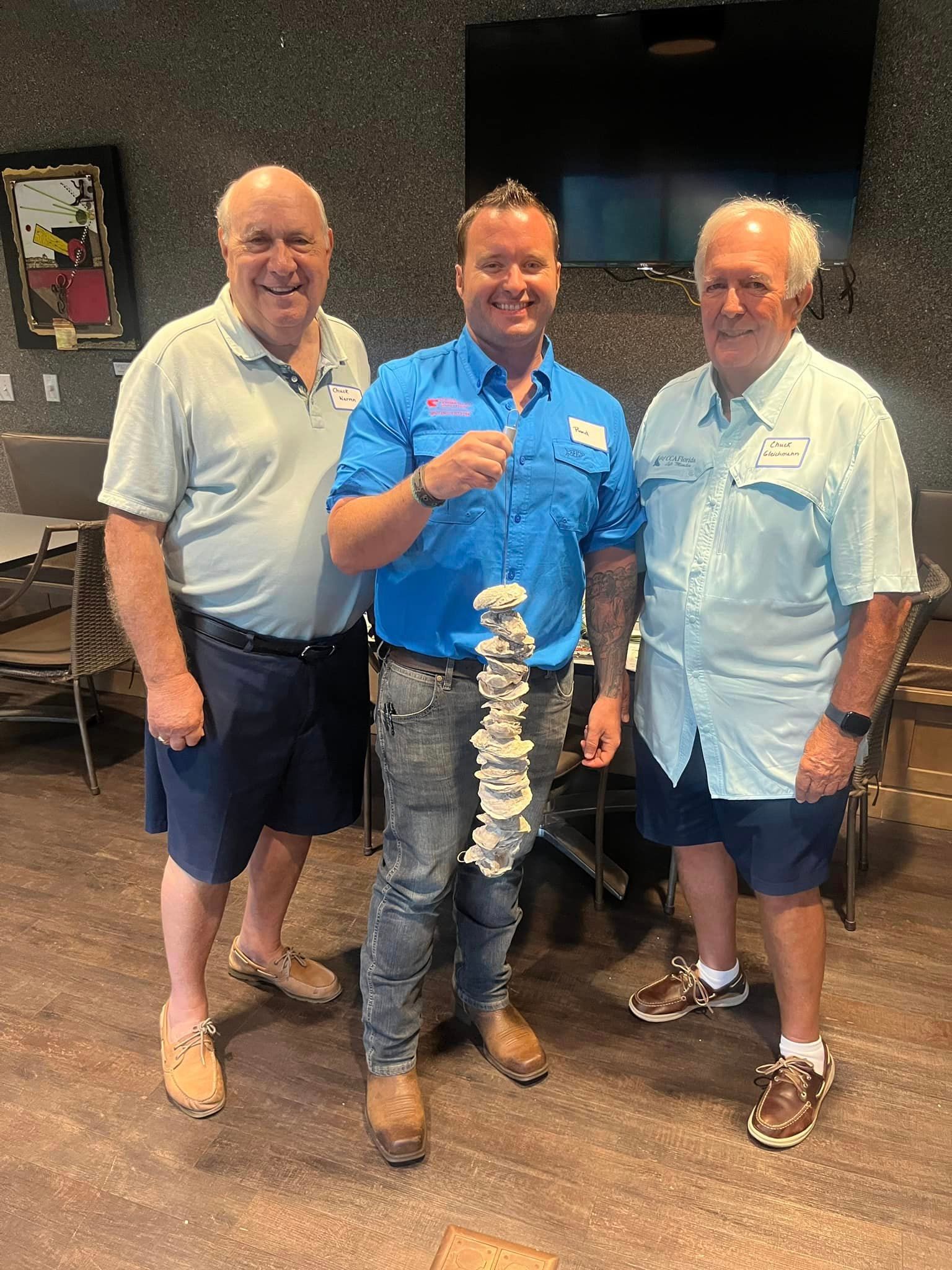Three men pose indoors, smiling beside a large trophy with a twisting white design.